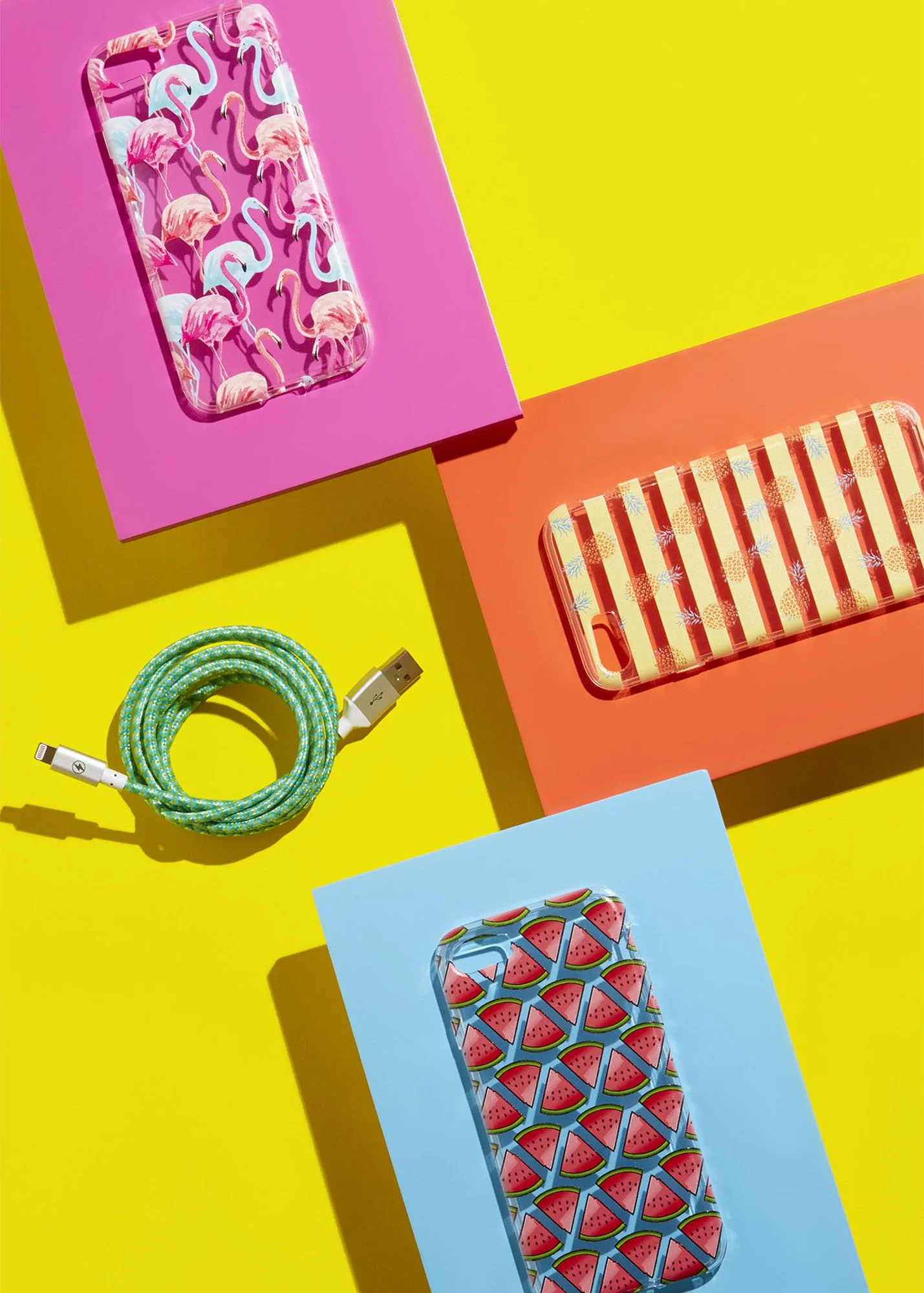 A colorful flat lay of three patterned portable phone chargers, a bright green USB cable, and two pink and orange boxes on a vibrant yellow background.