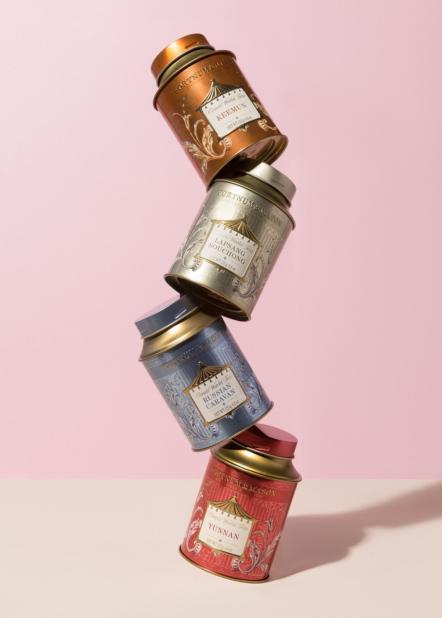 Stack of five colorful tea tins with intricate designs, arranged vertically against a pink background.