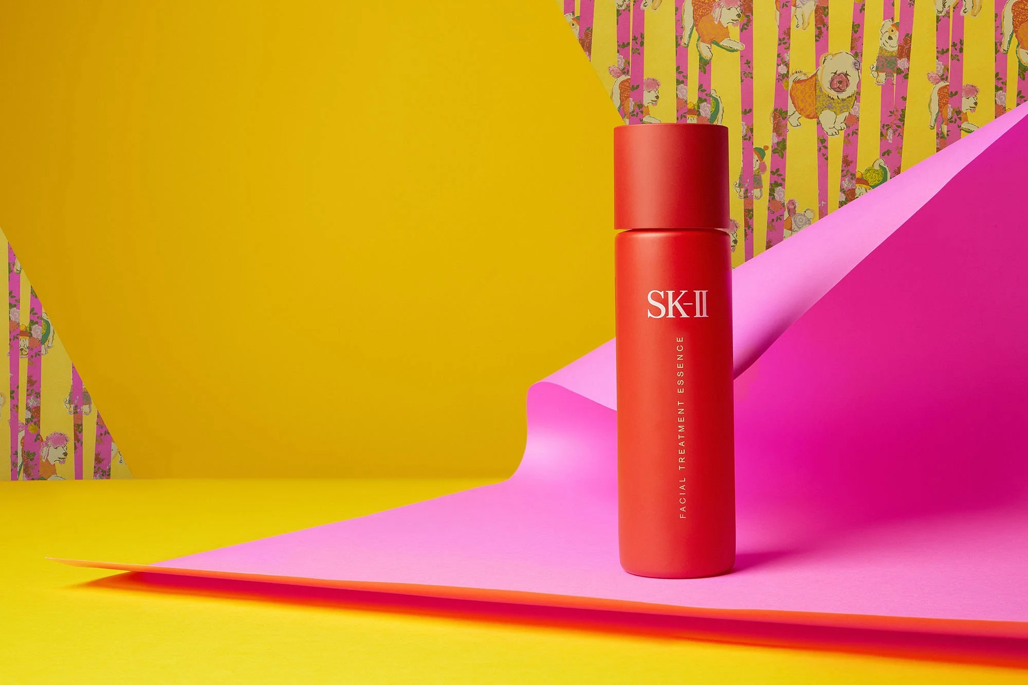 A red bottle of SK-II Facial Treatment Essence sitting on pink and yellow paper with a colorful, patterned background.