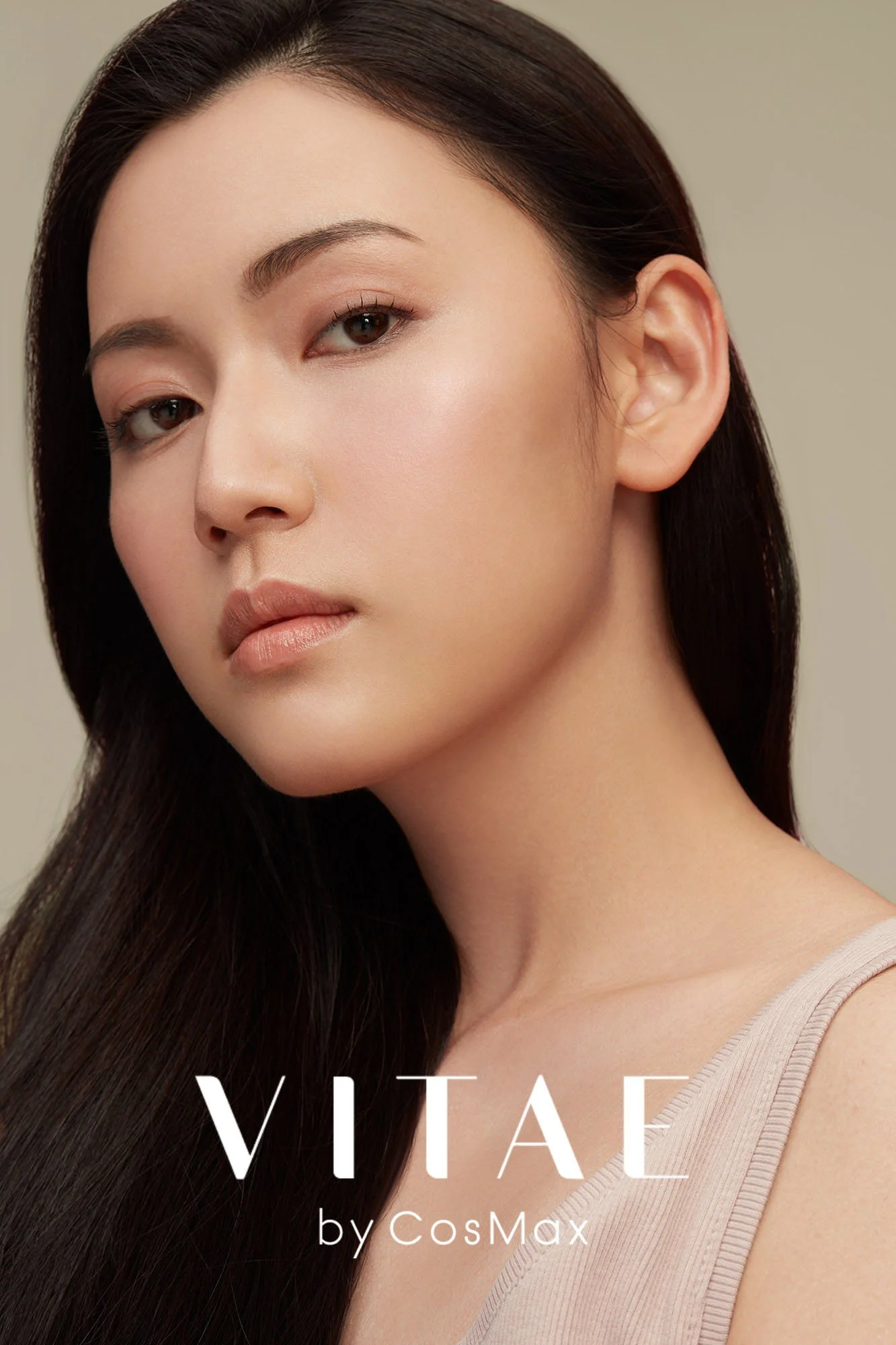Close-up of a young woman with long dark hair, natural makeup, and light skin, looking directly at the camera. The text on the image reads "VITAE by CosMax."