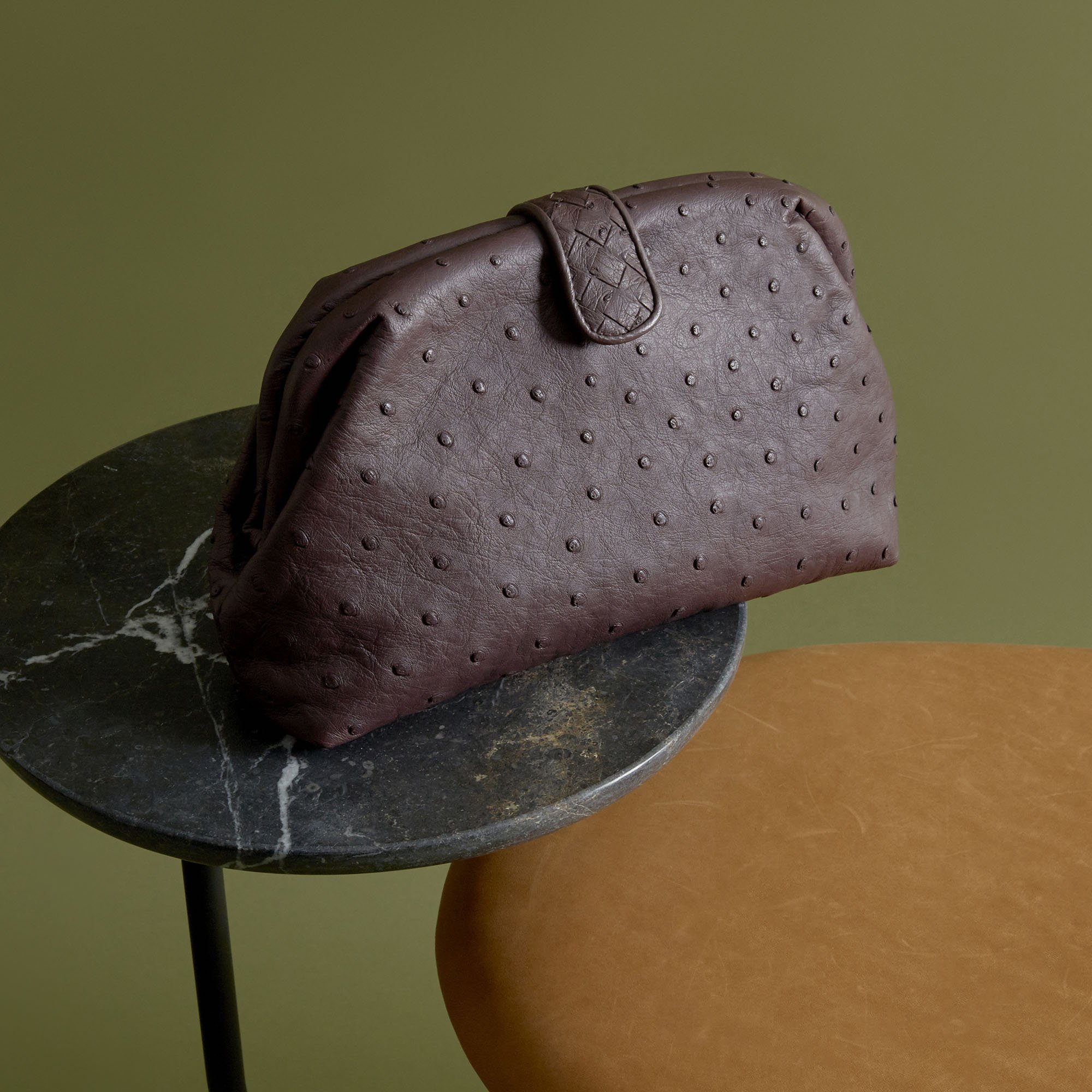 A brown leather handbag with a textured, dotted pattern resting on a black marble side table.