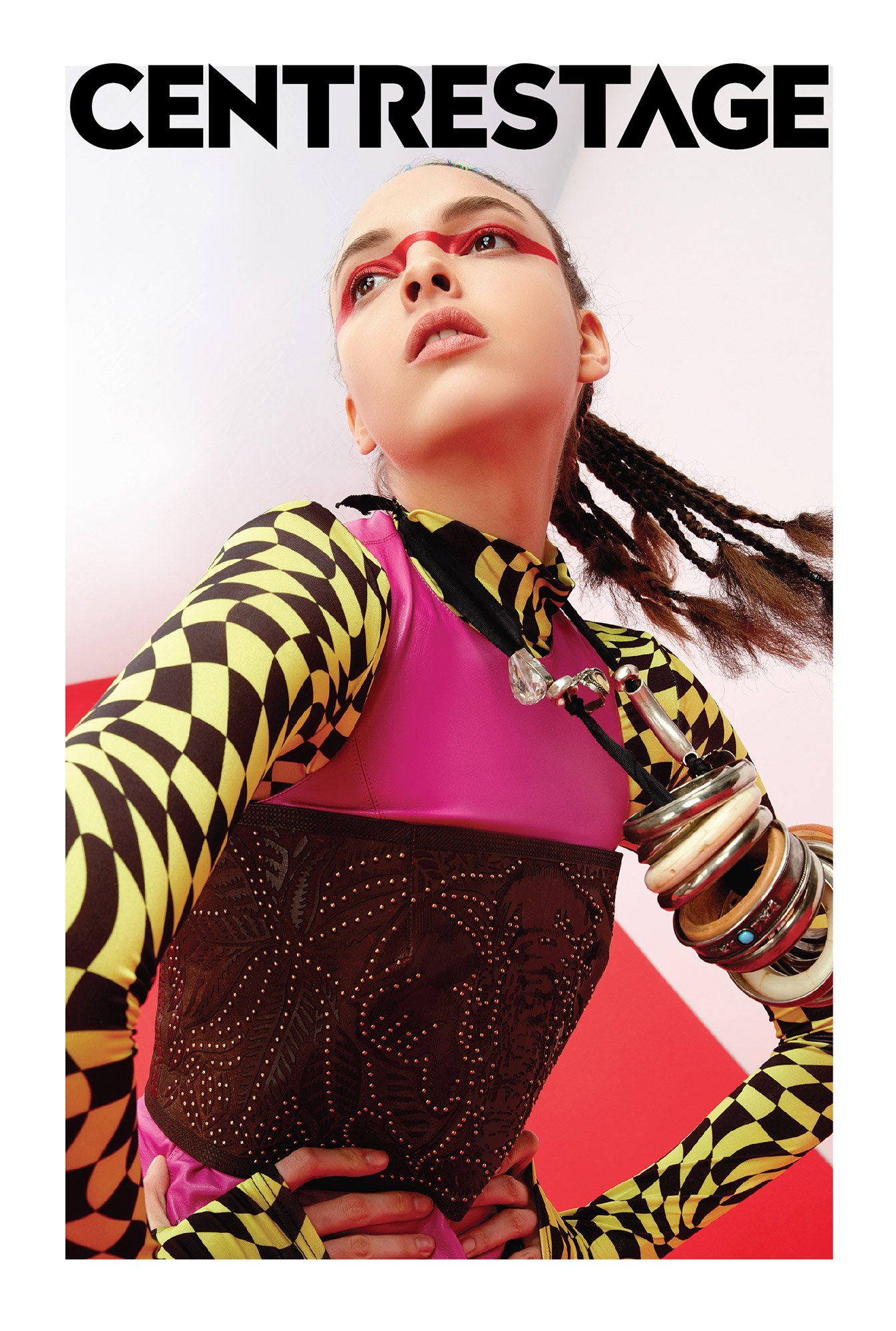 Young woman with braided hair wearing bold makeup, a colorful patterned outfit, and multiple bracelets, posing with a confident expression against a red and white background.