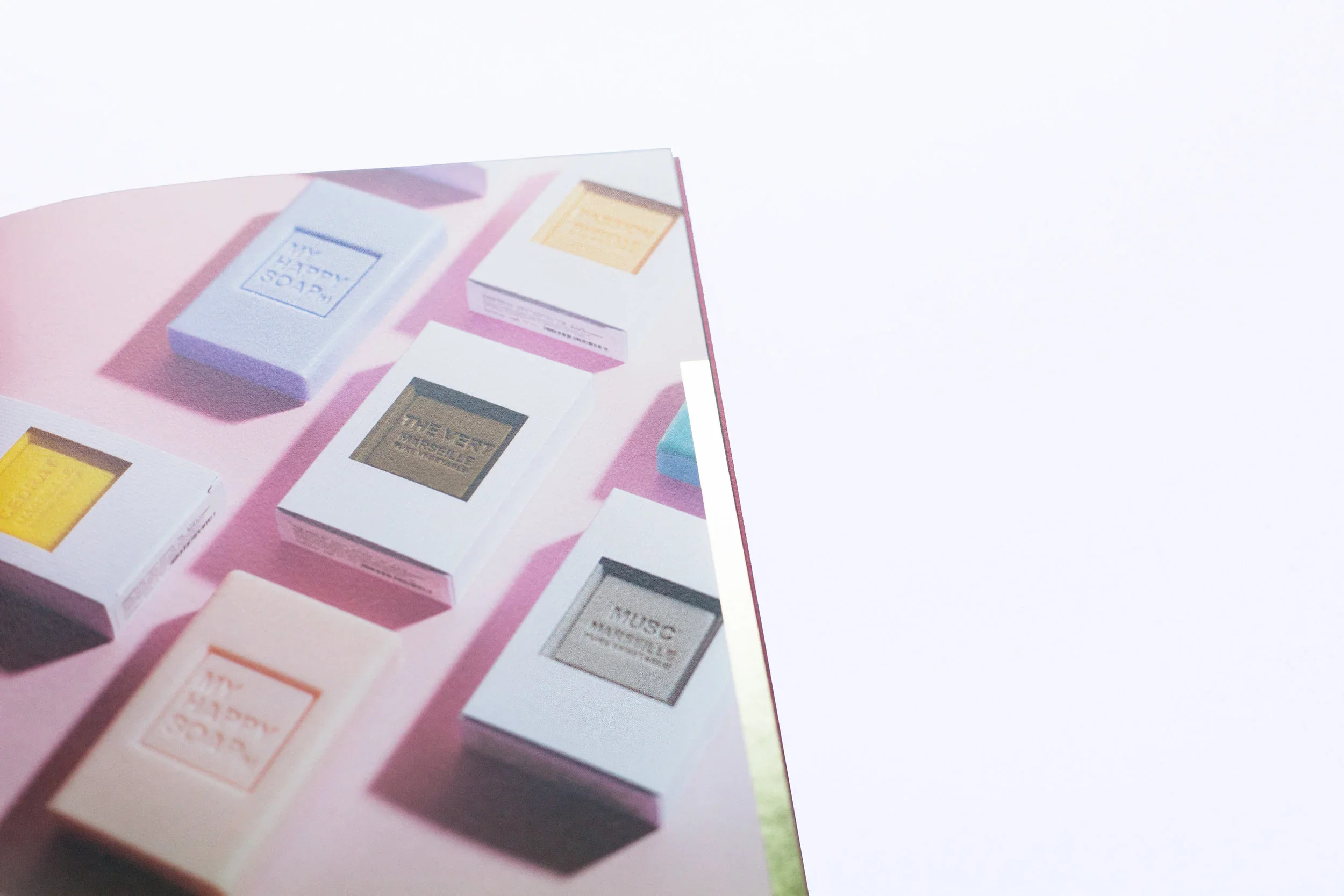 Various pastel-colored soap bars in white boxes displayed on a pink surface.