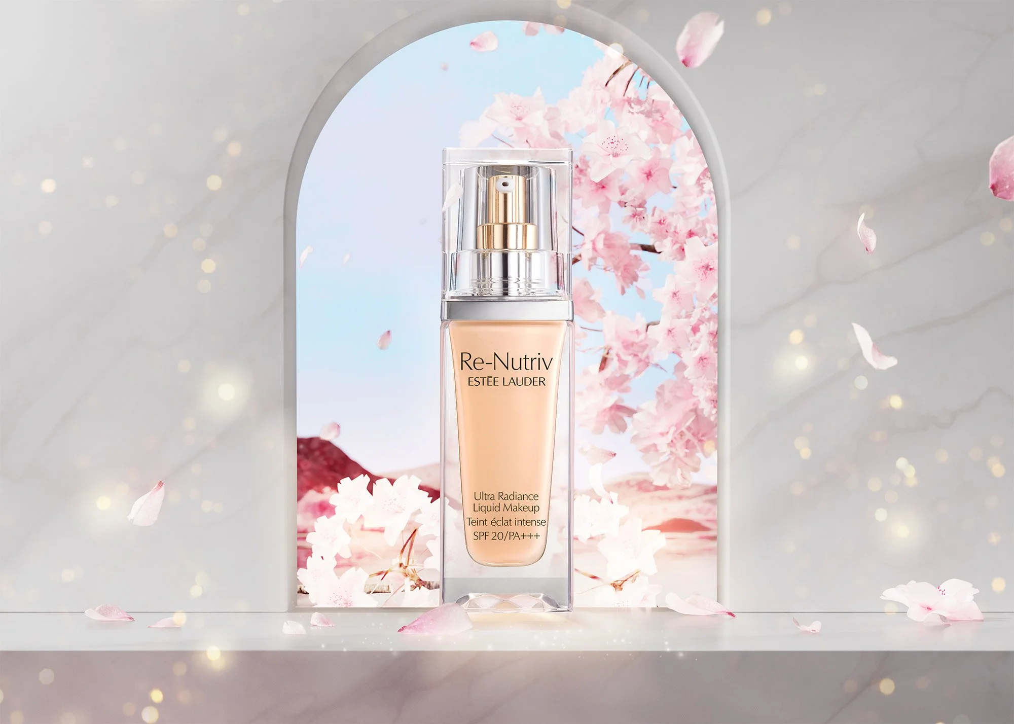 A bottle of Estée Lauder Re-Nutriv Ultra Radiance Liquid Makeup displayed in front of a pink floral backdrop with cherry blossoms and a mountain, framed by an arched opening, with falling cherry blossom petals around.