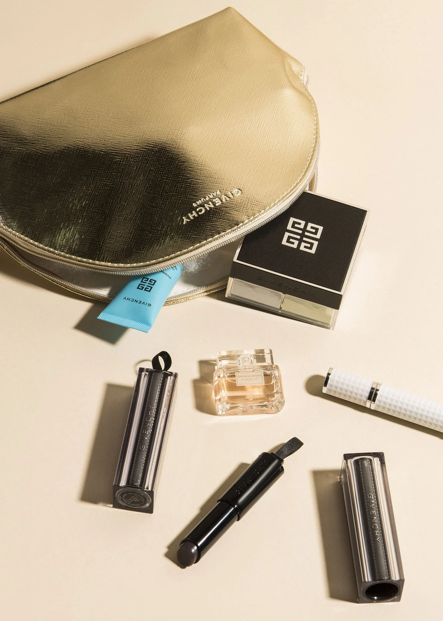 A collection of luxury cosmetics and skincare products with a gold Givenchy makeup bag on a light background.