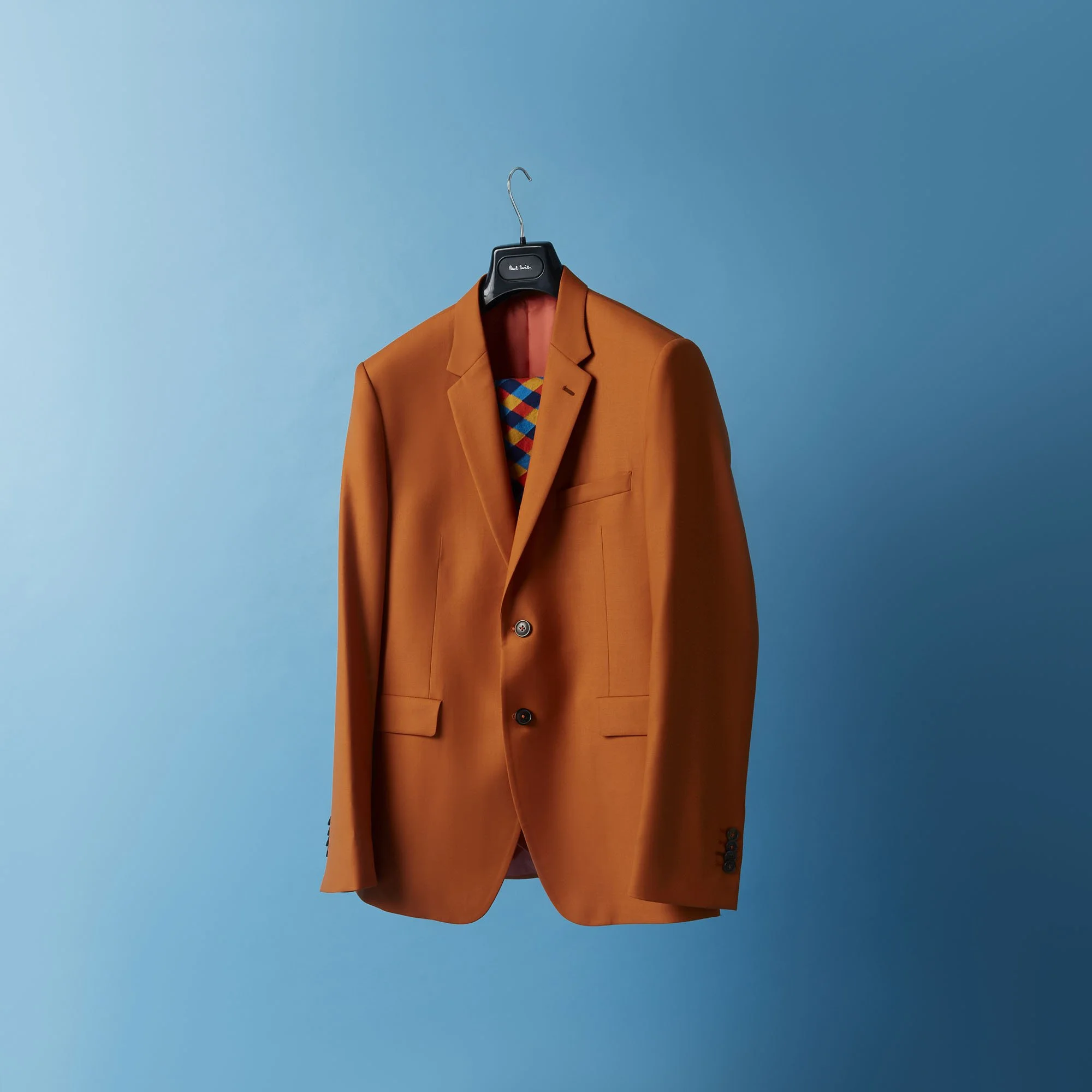 An orange suit jacket hanging on a black hanger against a blue background.