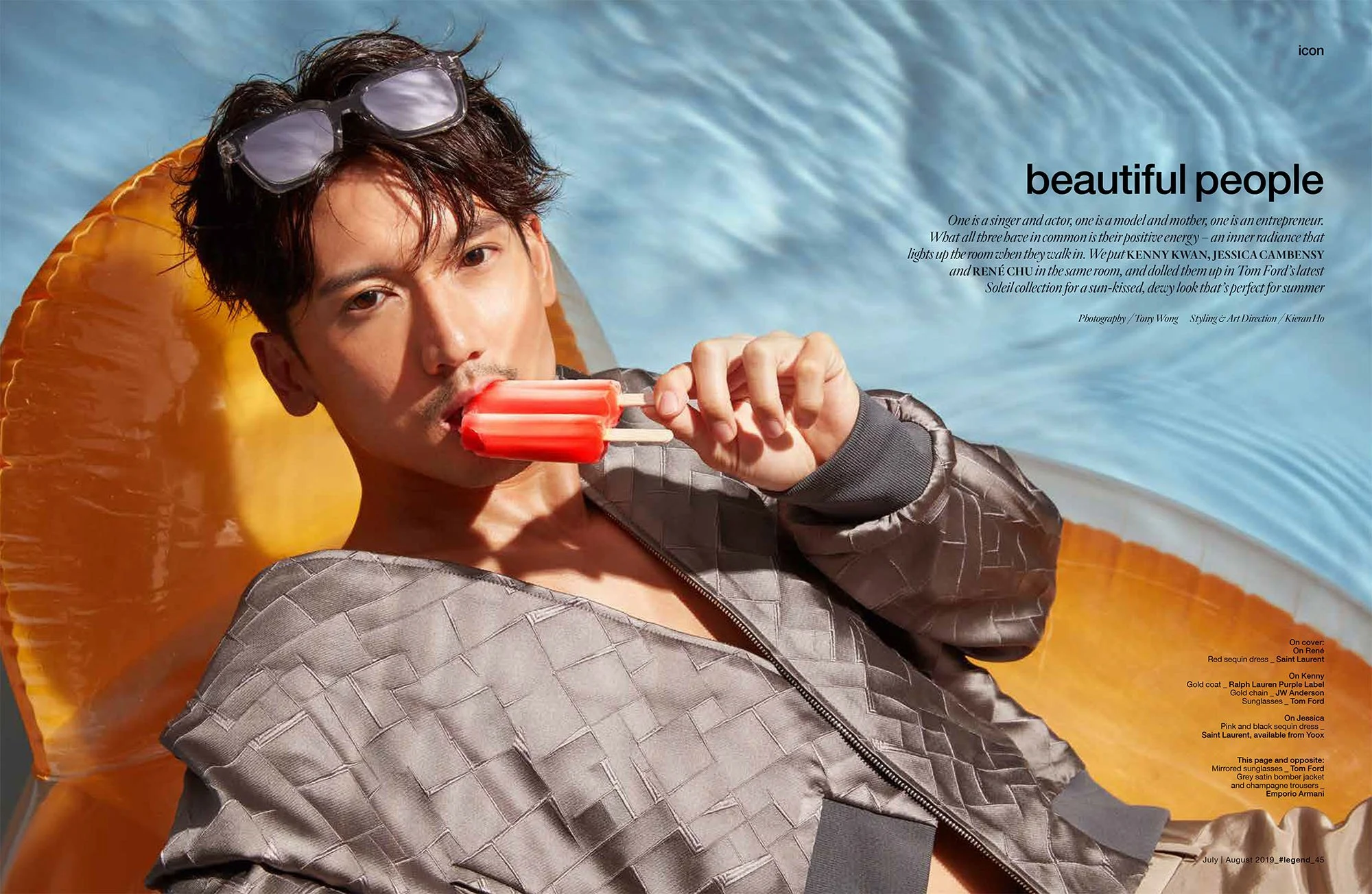 Man lying on a yellow float in a pool, holding a red popsicle, wearing sunglasses and a grey quilted bomber jacket.