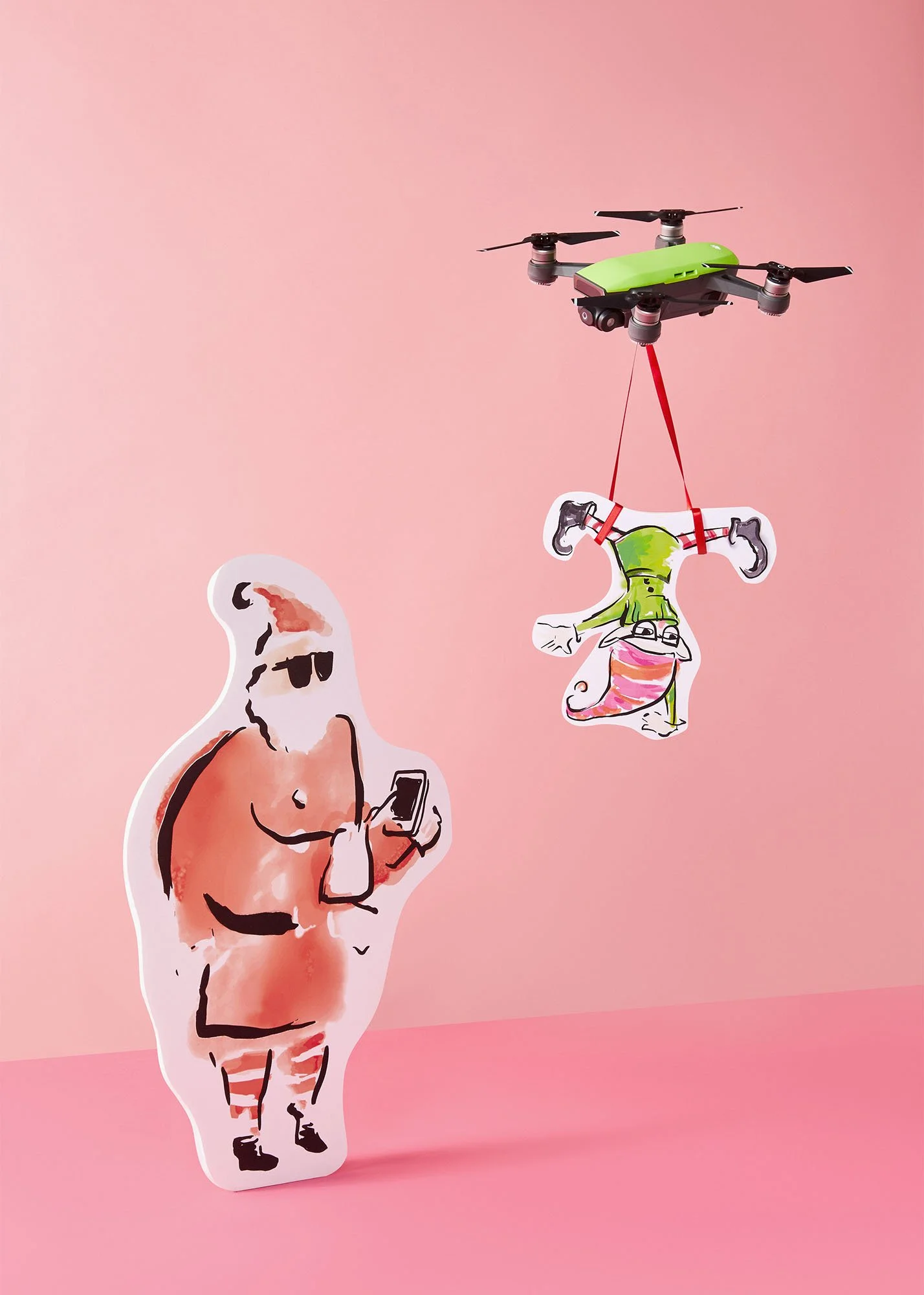 A small drone carrying a paper cutout of a girl in a green outfit and glasses, suspended by a red string, against a pink background. There is also a cardboard cutout of a man wearing sunglasses looking at his phone.
