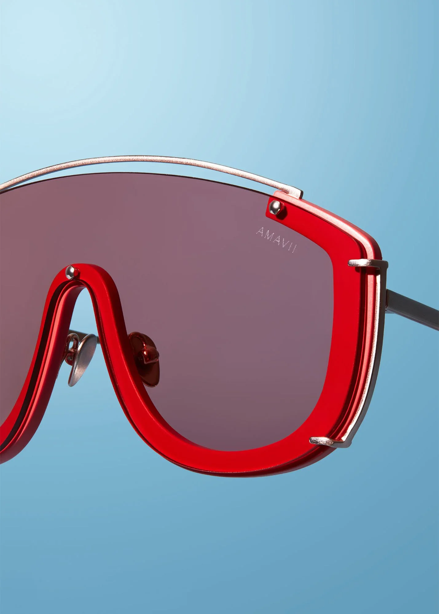 Close-up of sunglasses with red frames and gray lenses against a light blue background.