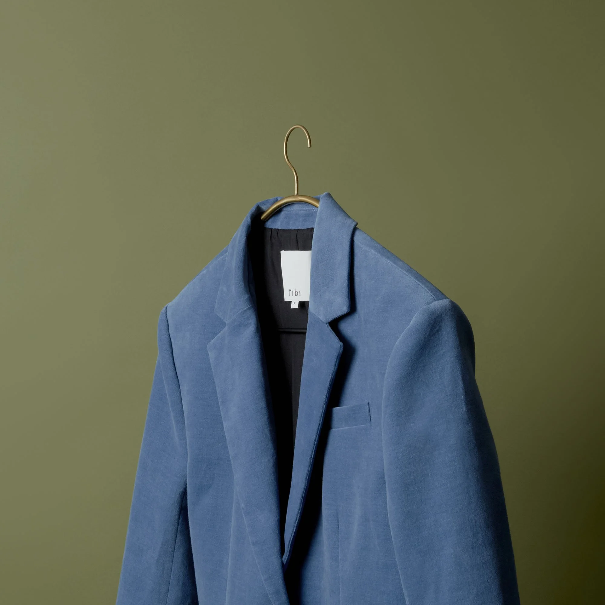 Blue blazer hanging on a gold hanger against an olive green background.