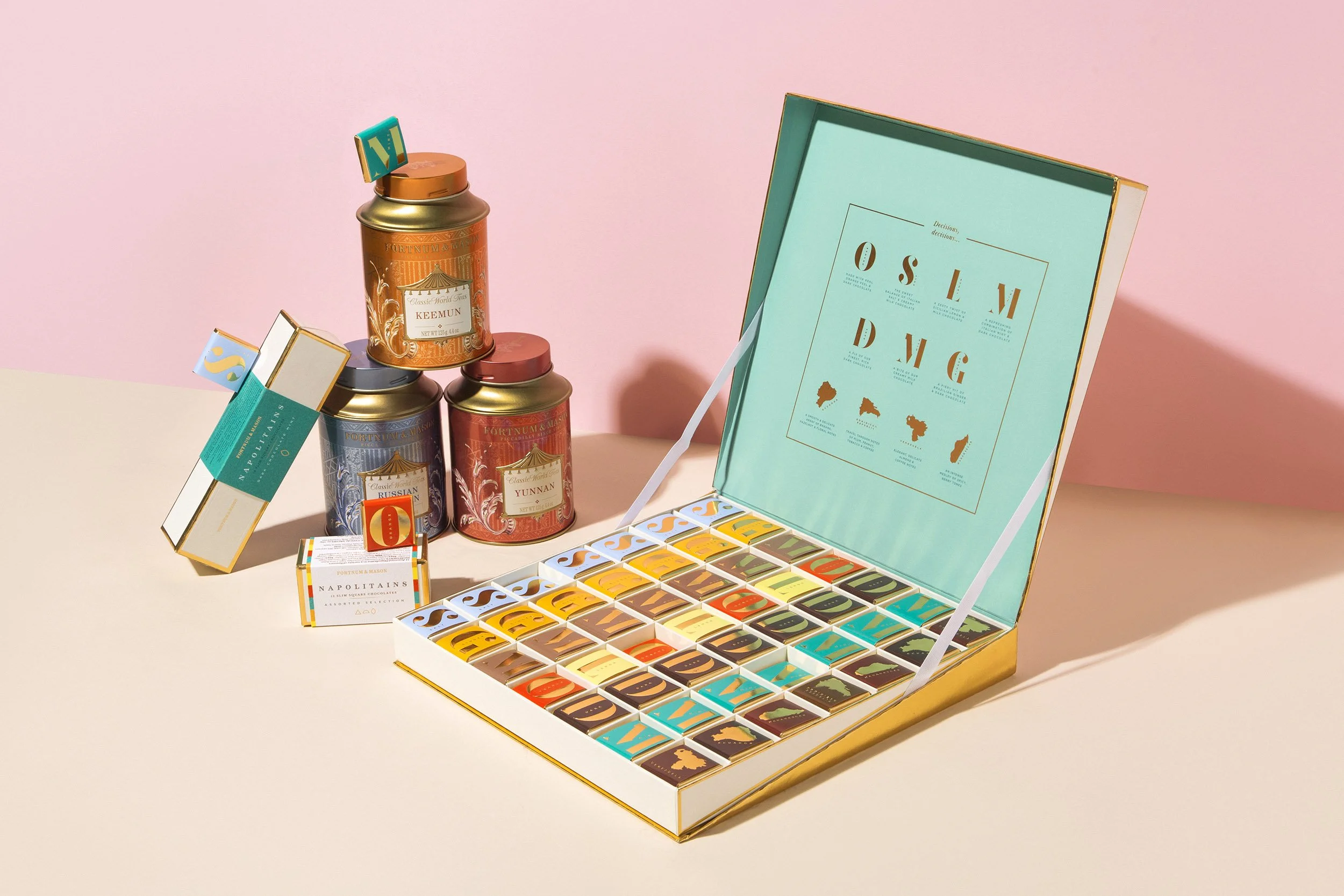 A colorful box of assorted artisanal chocolates with individual chocolate squares in a variety of colors and designs, along with decorative tins and packaging.