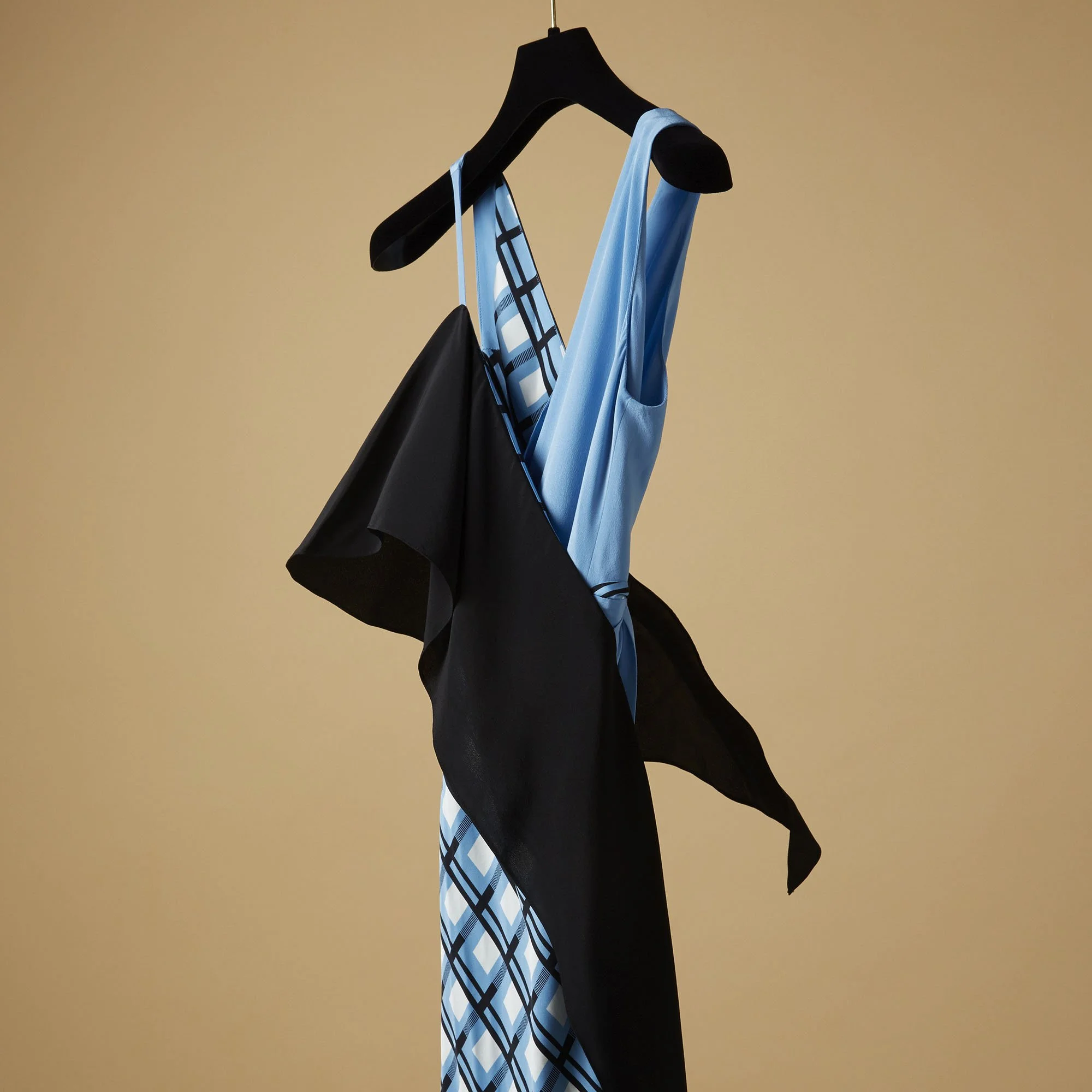 A black hanger holding a blue and black dress with a geometric pattern, draped with a black jacket against a beige background.