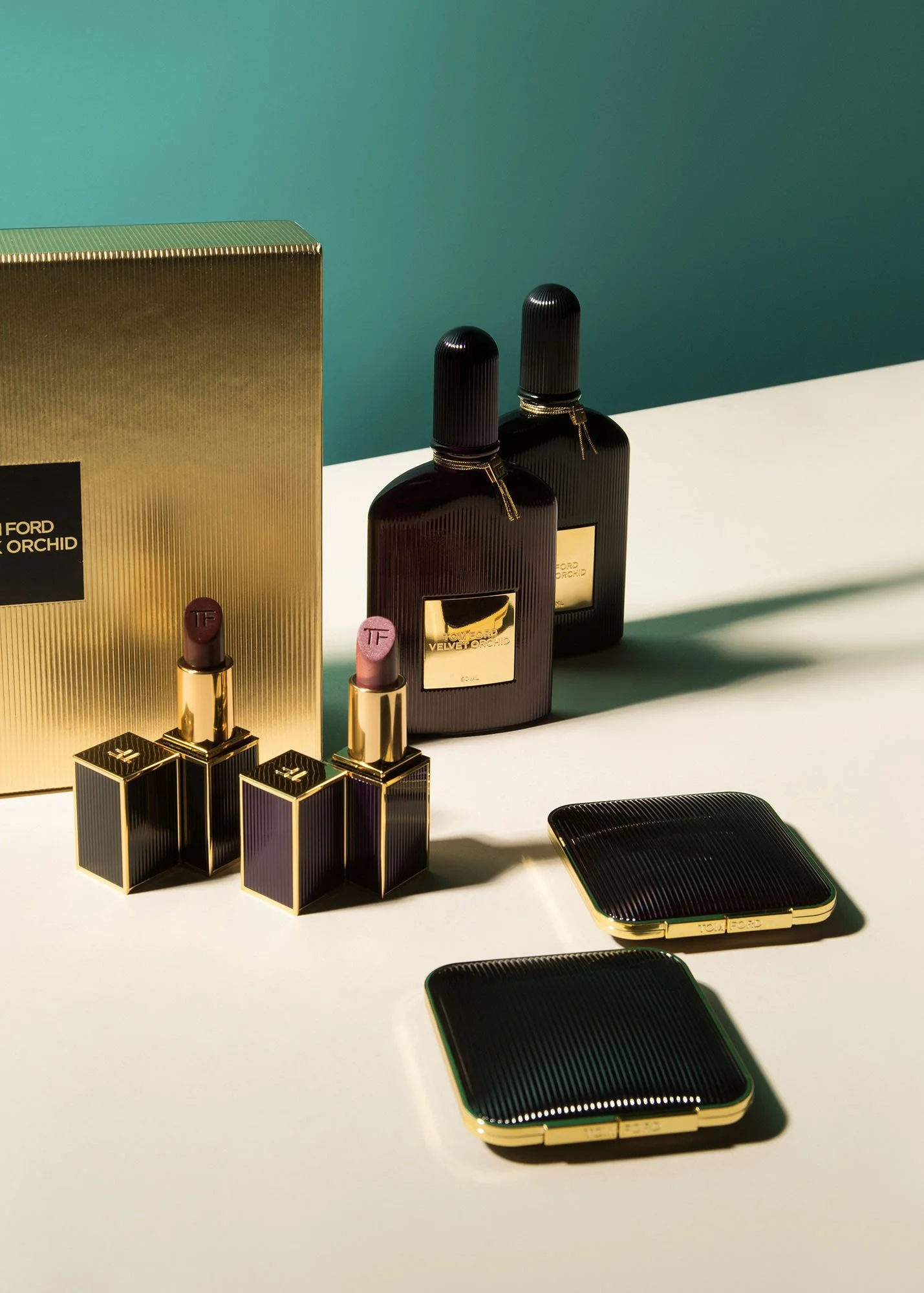 Luxury perfume bottles and lipsticks with gold accents on a white surface, with a gold and black box in the background.