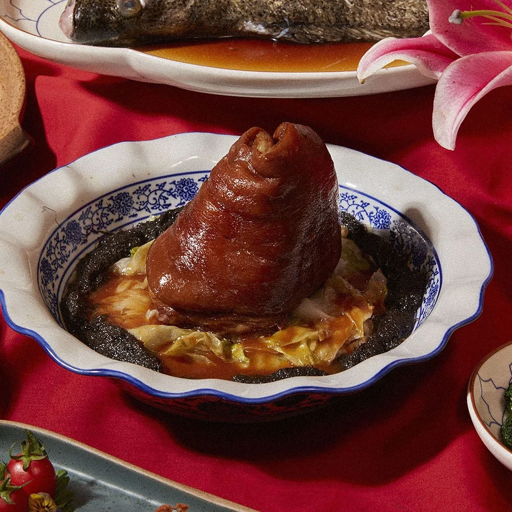 A bowl with a pig's trotter served on top of vegetables and black fungus in a patterned dish.
