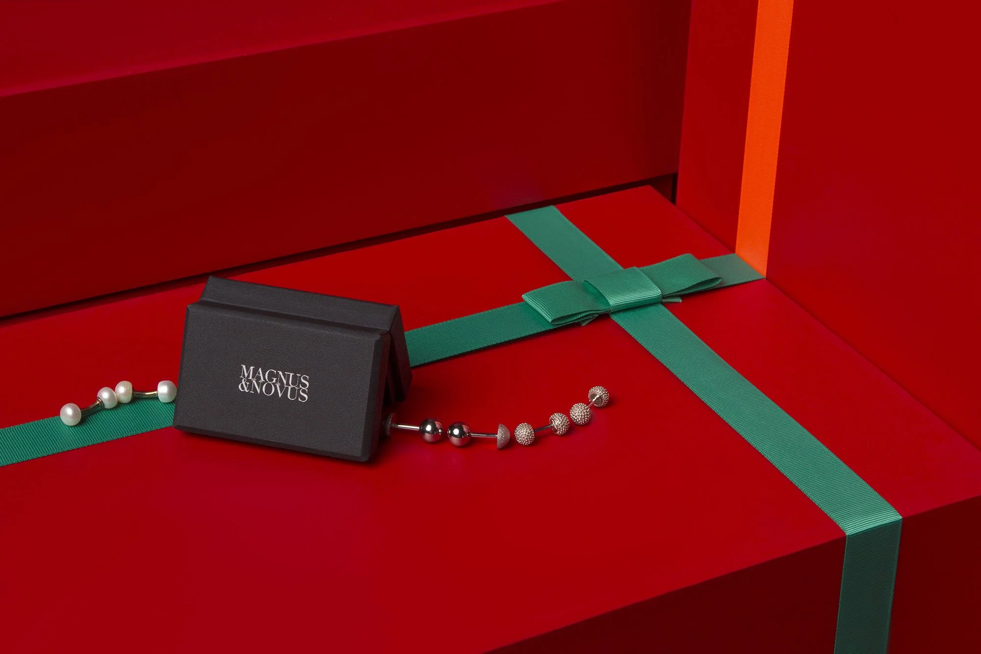 Red gift box with green ribbon, showcasing jewelry including a pearl necklace and a silver beaded bracelet.