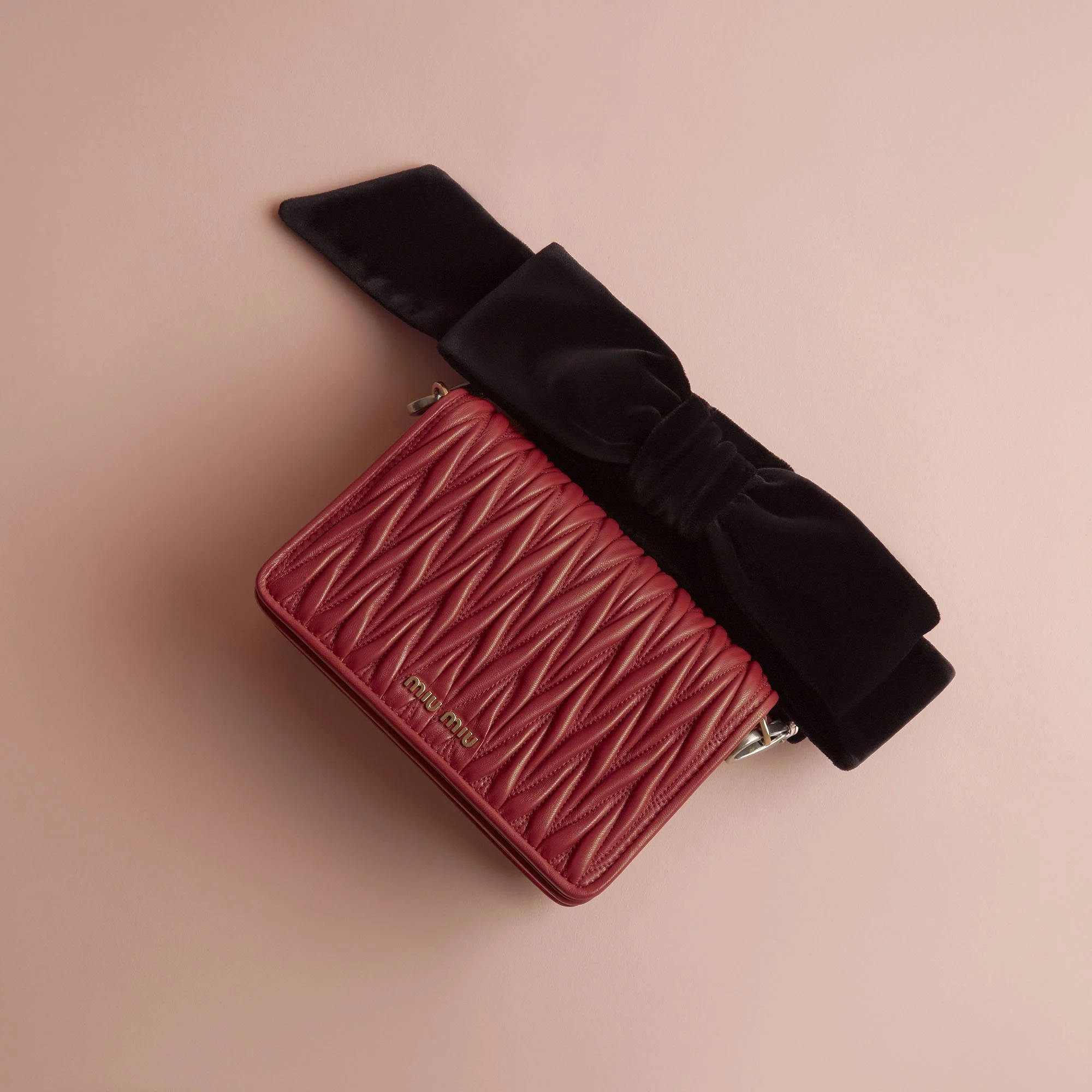 A pink quilted Miu Miu handbag with a black velvet bow handle against a pink background.
