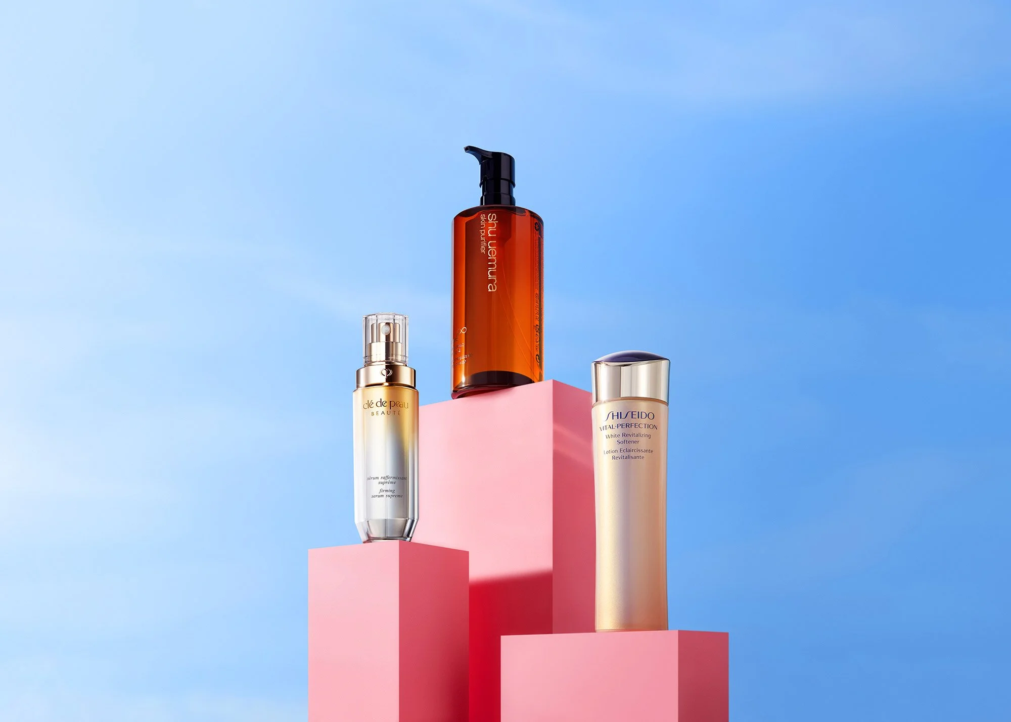 Three skincare bottles placed on pink pedestals against a blue sky background.
