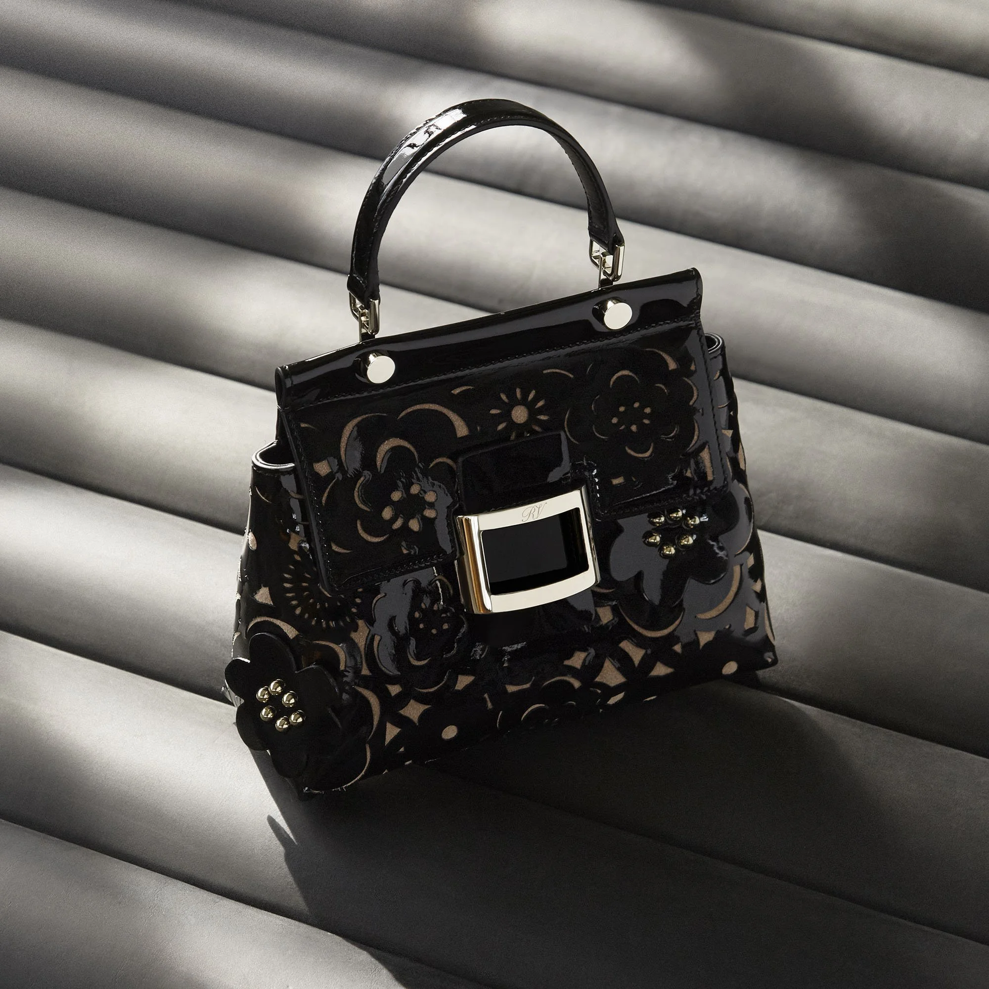 A black handbag with floral cutout design and gold accents on a gray surface.
