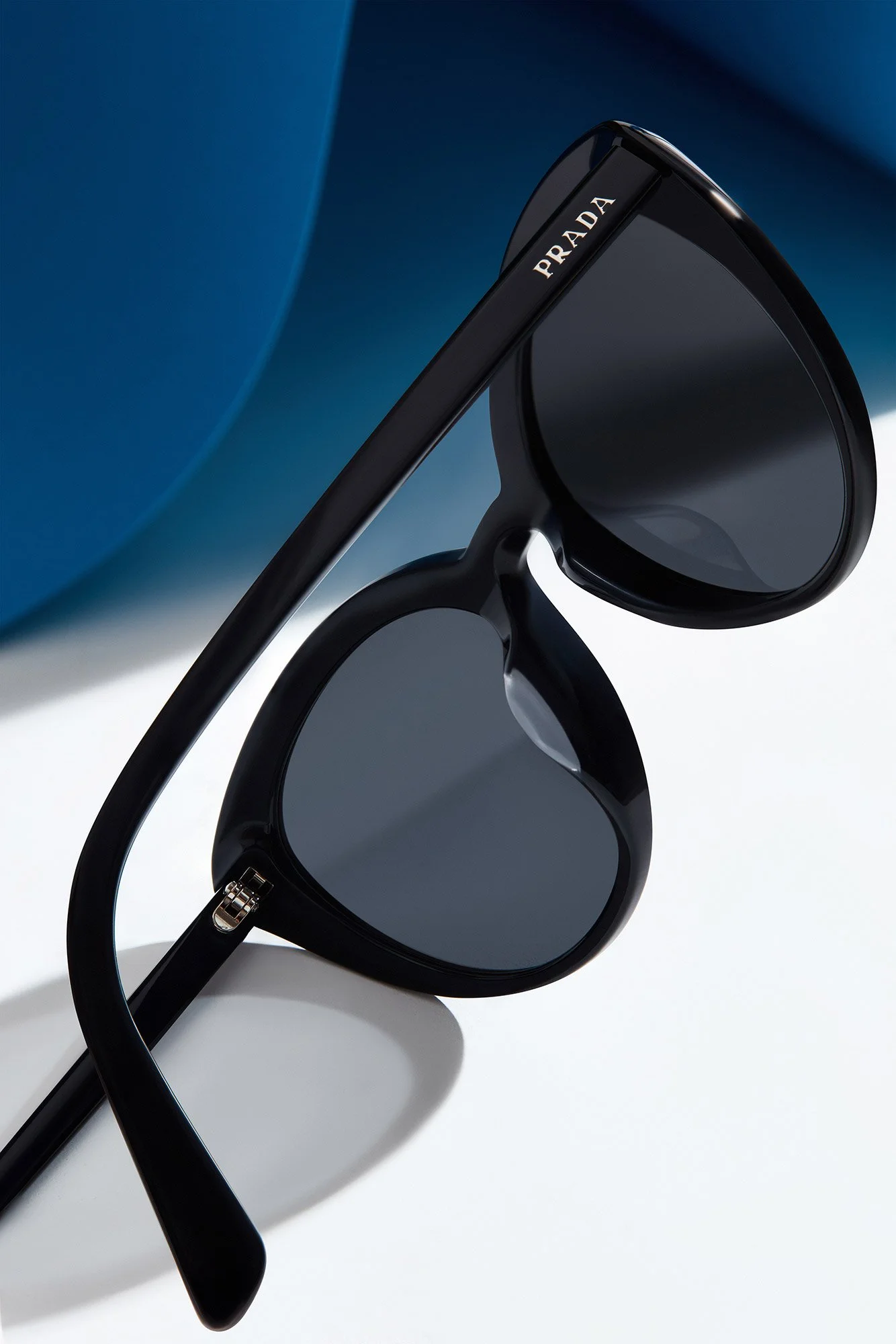 Black Prada heart-shaped sunglasses on a white surface with a blue background.