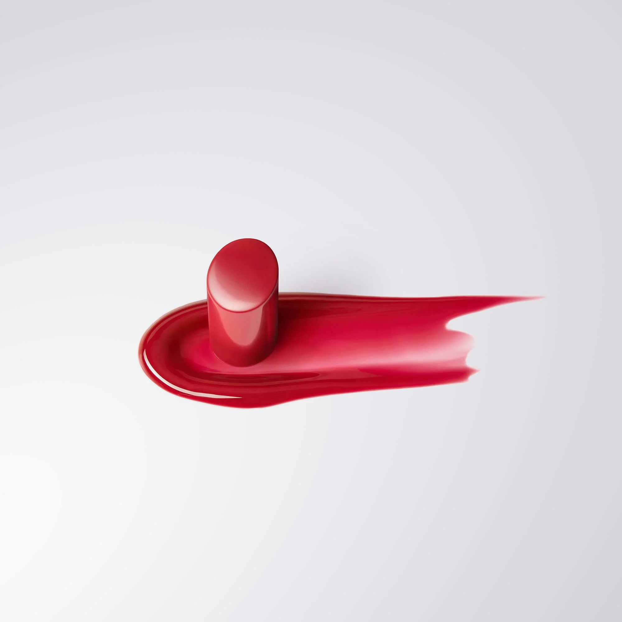 A single red lipstick with a smooth, rounded top is placed upright on a flat surface, with a smear of bright red lipstick spread around its base.