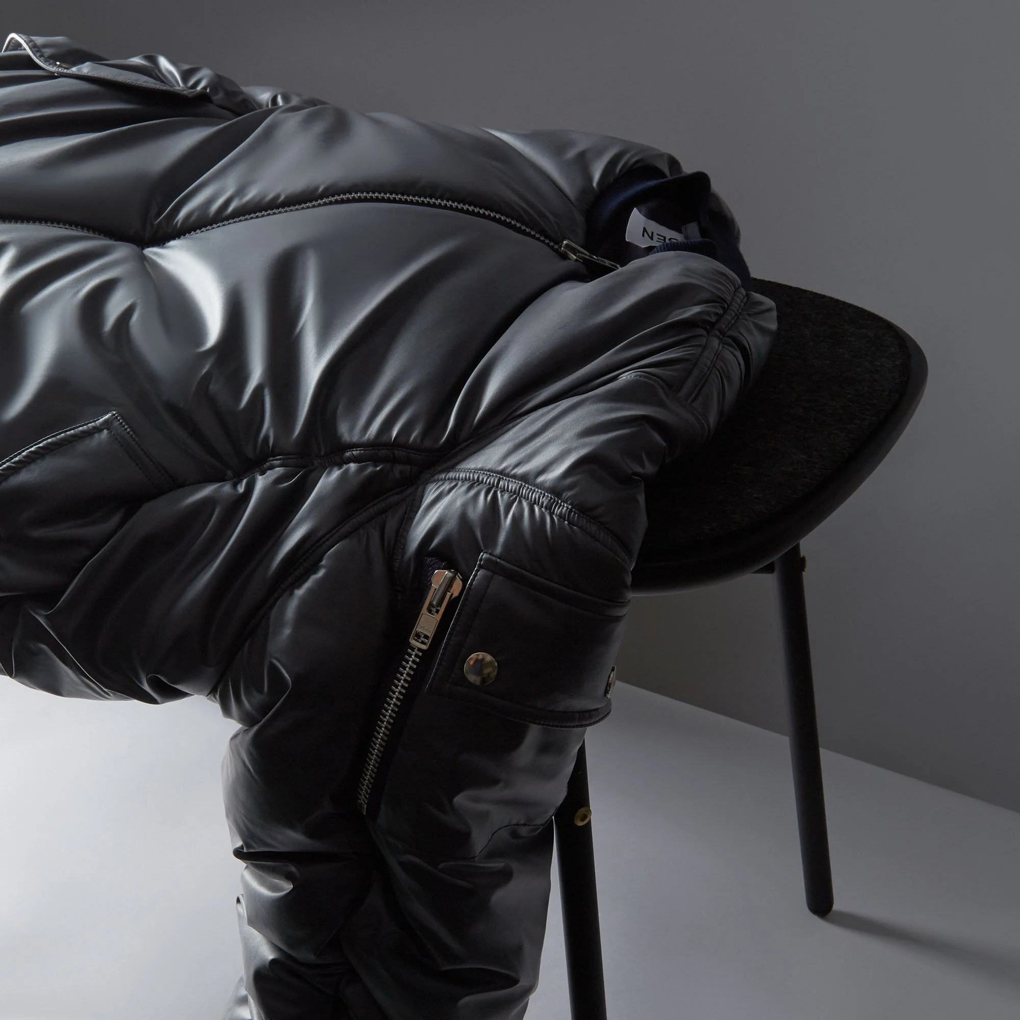 Close-up of a black leather jacket draped over a black chair against a gray wall.