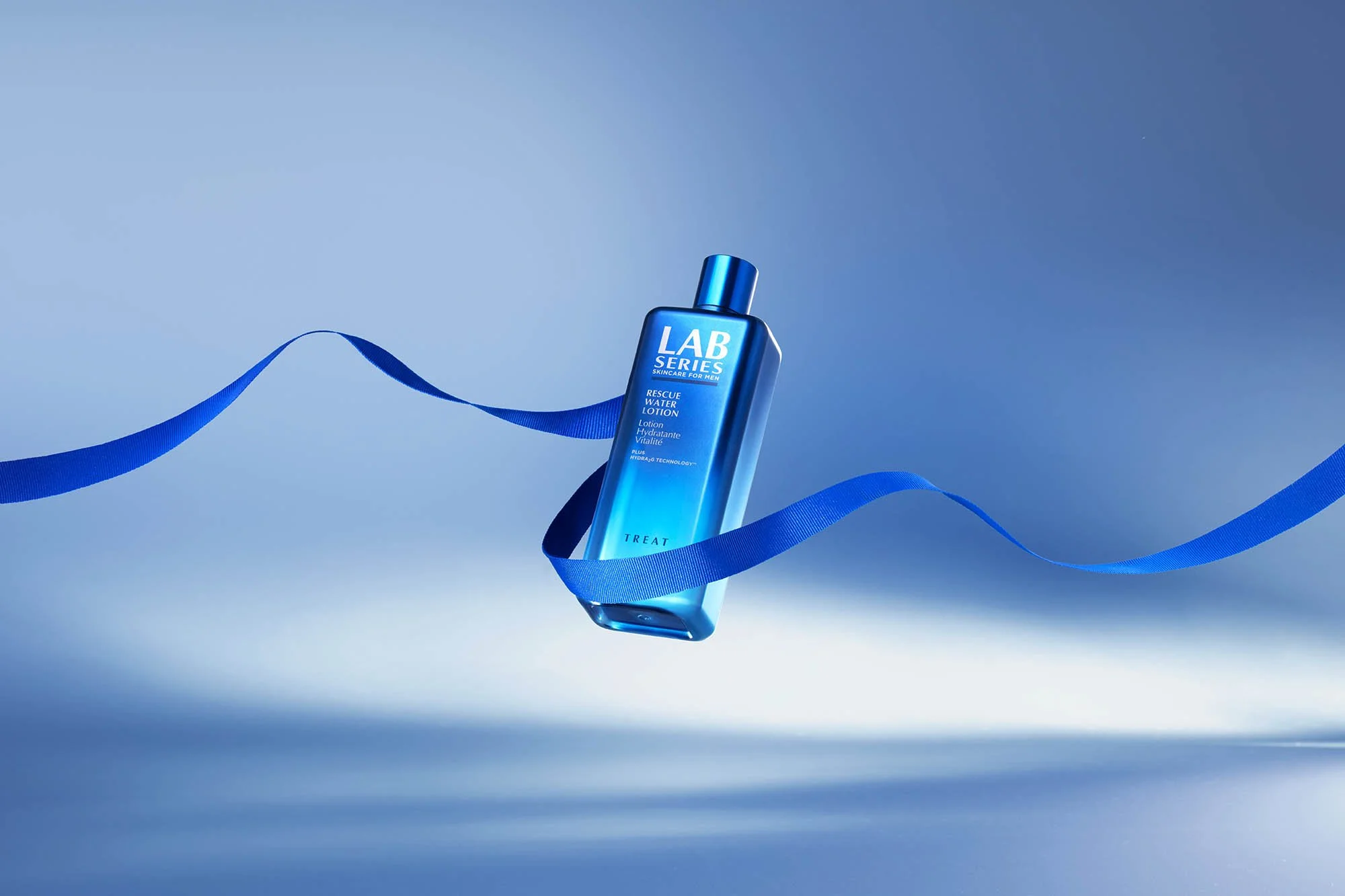 Blue bottle of Lab Series skincare product called Rescue Water Lotion with a blue ribbon flowing around it on a light blue background.