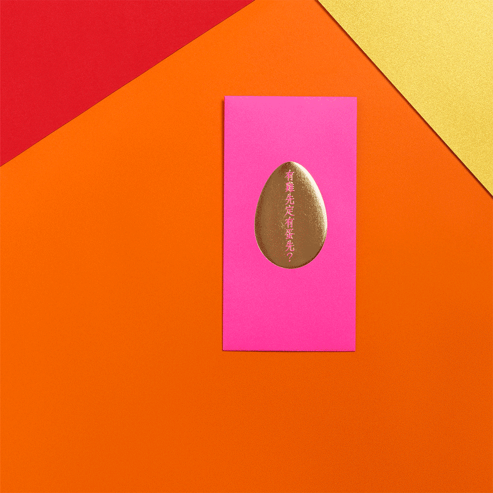 A gold-colored egg with pink Chinese characters on it, placed on a pink rectangular background, surrounded by red, orange, and gold textured surfaces.
