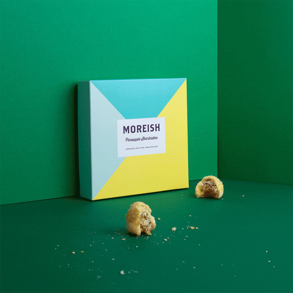 Box of Moreish pineapple shortcakes with two pieces broken apart on green background.