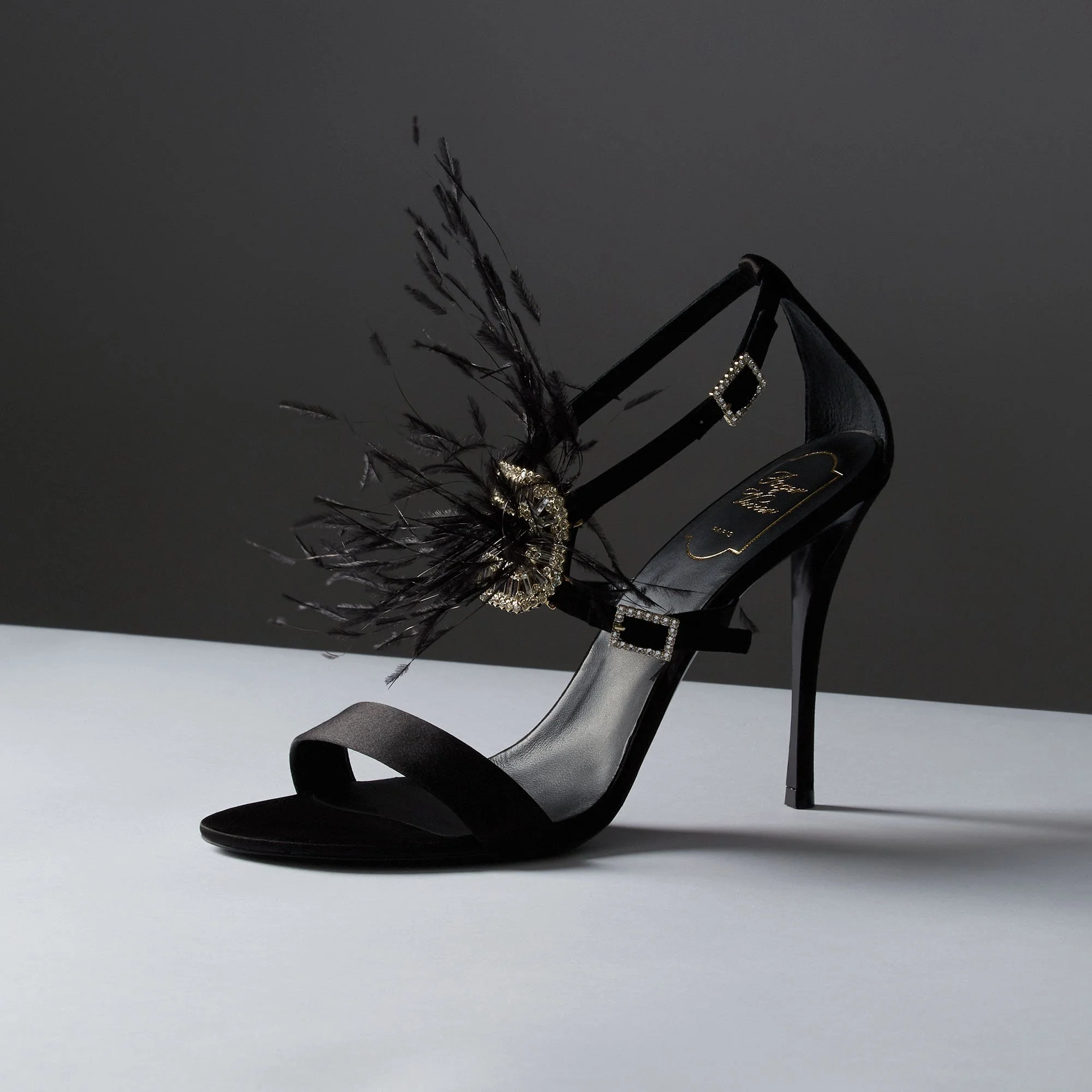 A black high-heeled sandal with decorative feathers and rhinestones adornment.