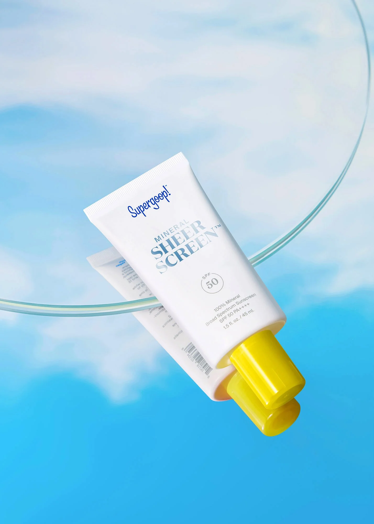 A tube of Supergoop! Mineral Sheer Screen SPF 50 broad-spectrum sunscreen floating near a glass fishbowl against a sky background.
