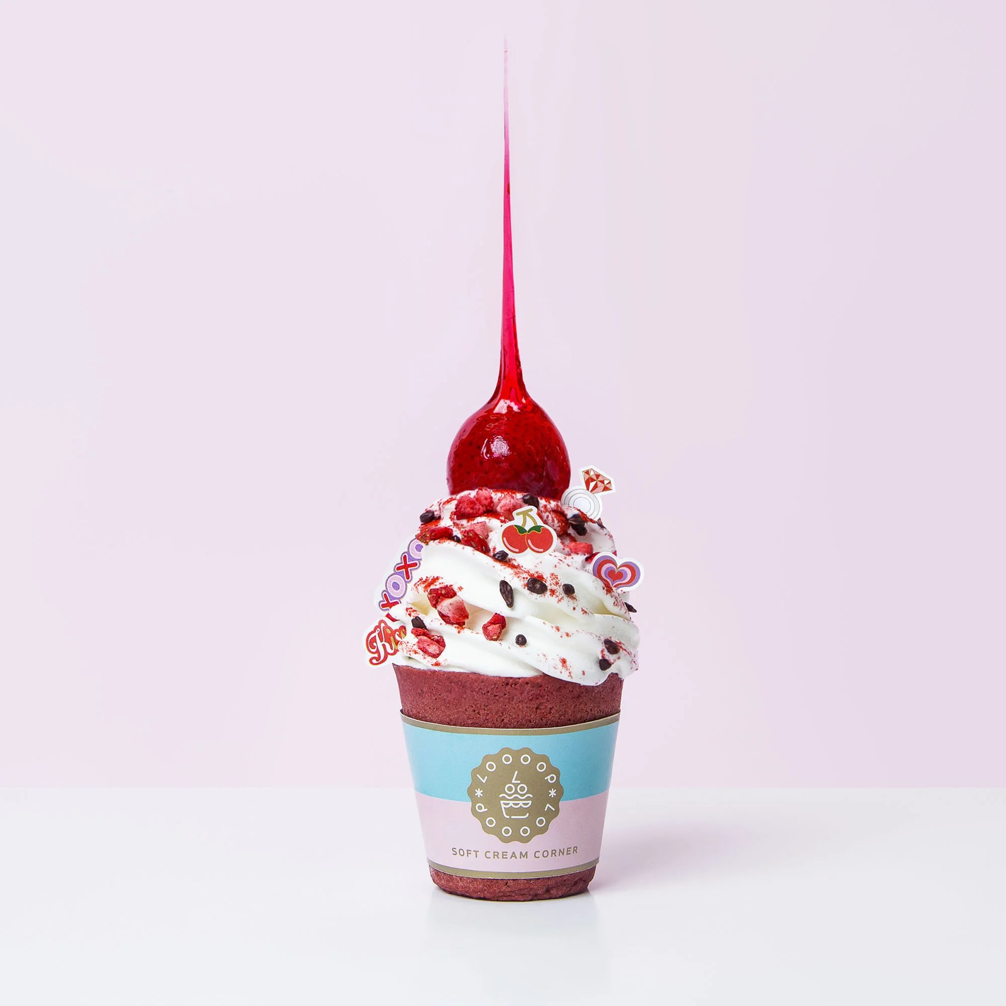 Ice cream cone with whipped cream, cherry topping, colorful sprinkles, and a cherry on top against a pink background.