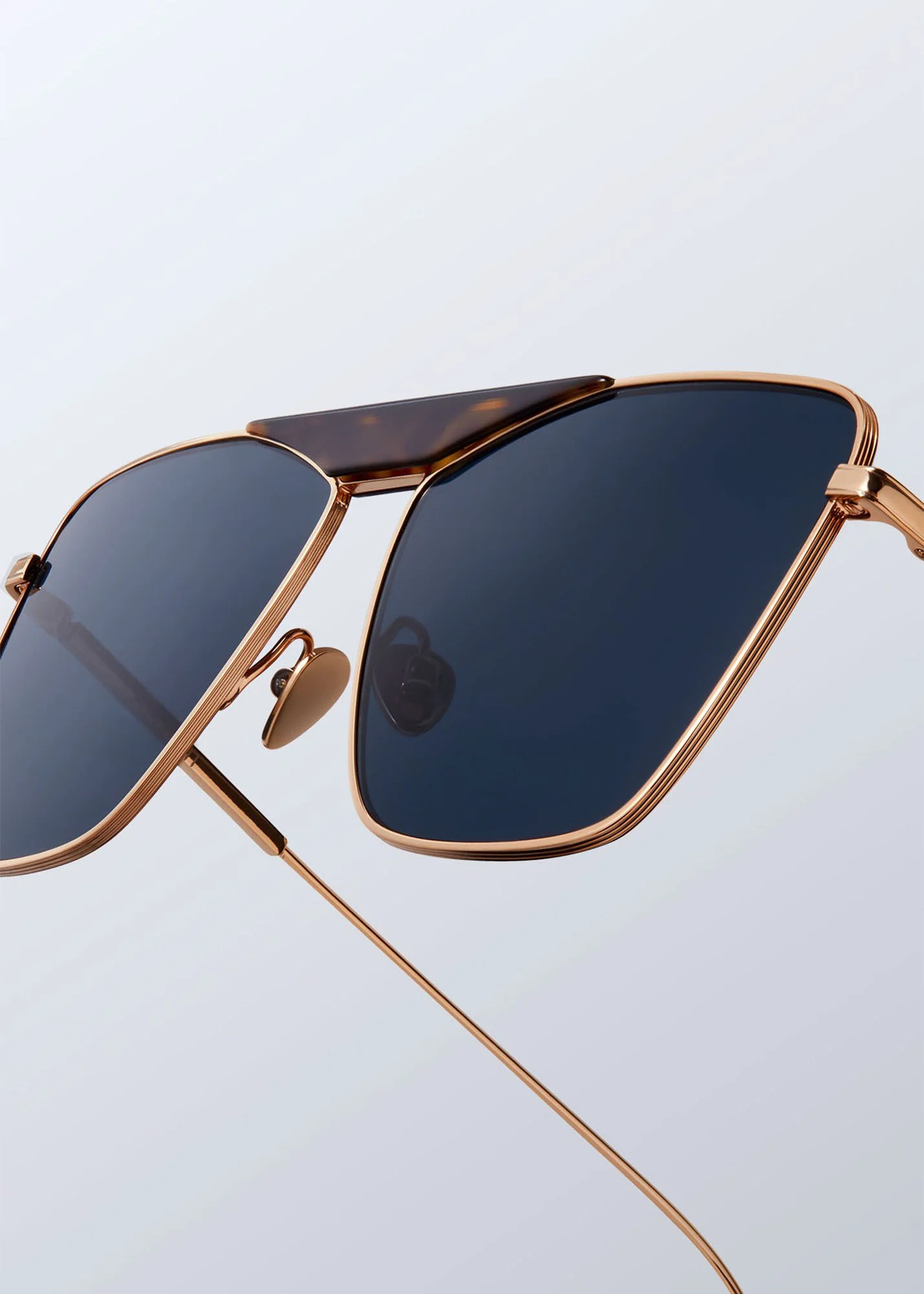 Close-up of a pair of sunglasses with dark lenses and a gold frame, set against a plain light background.