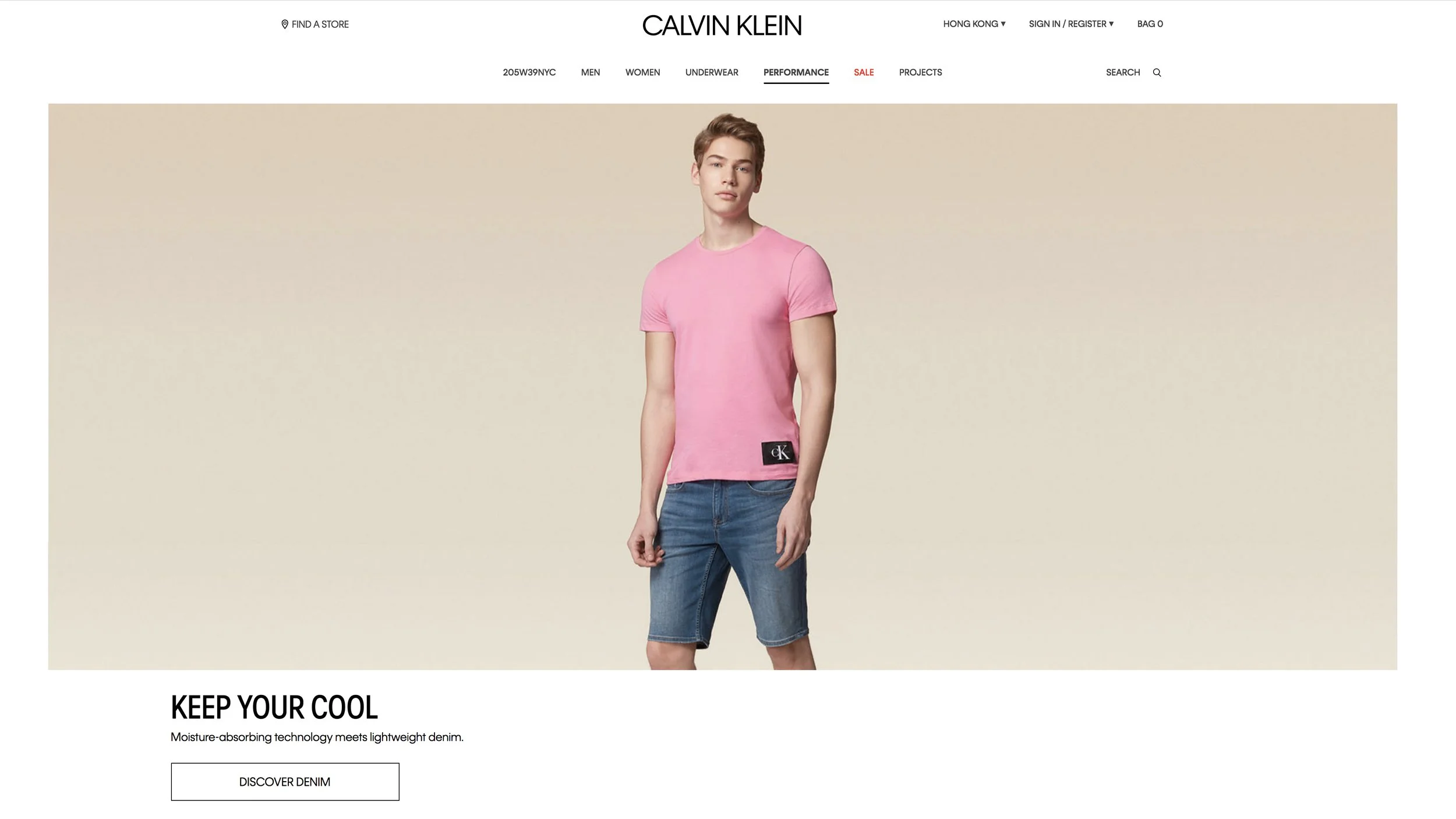 A male model wearing a pink T-shirt and denim shorts standing against a beige background, featured on a Calvin Klein online store webpage.