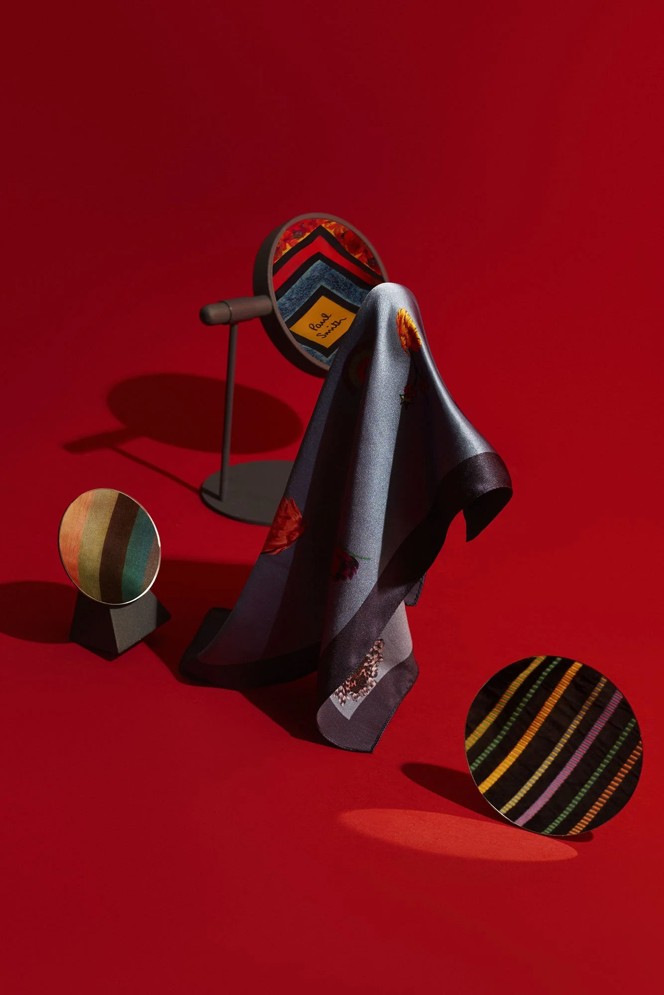Display of textile samples with colorful stripes, a scarf with floral patterns, and a small stand showcasing fabric color swatches against a red background.