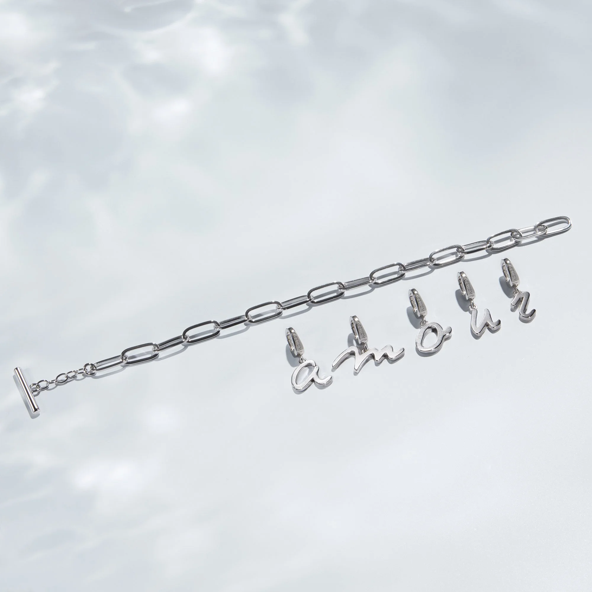 A silver bracelet with chain links and a charm spelling 'among' hanging from the links.