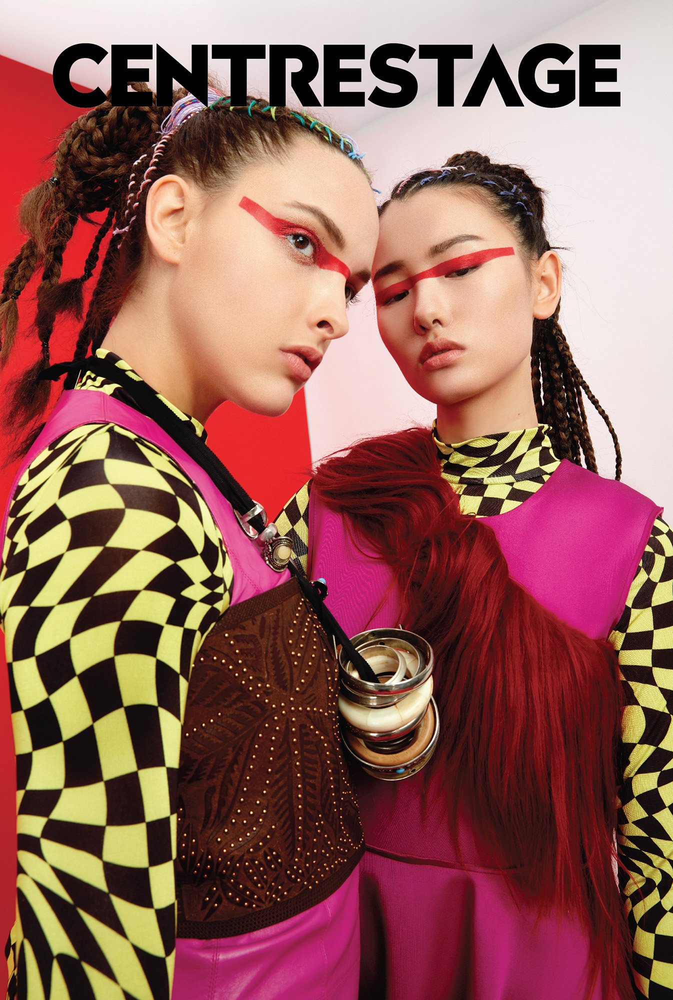 Two models with creative makeup and colorful clothing standing close together against a vibrant background, with the word 'CENTRESTAGE' at the top.