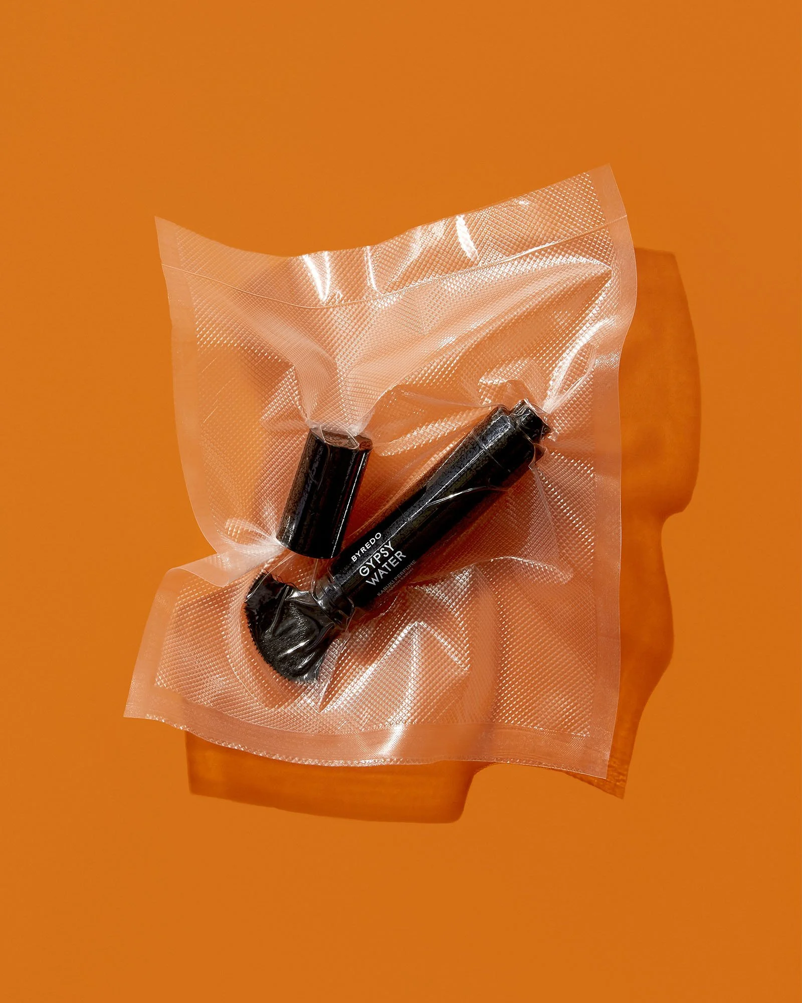 Two black lipstick tubes labeled "Byredo Gypsy Water" inside a clear, sealed plastic bag on an orange background.
