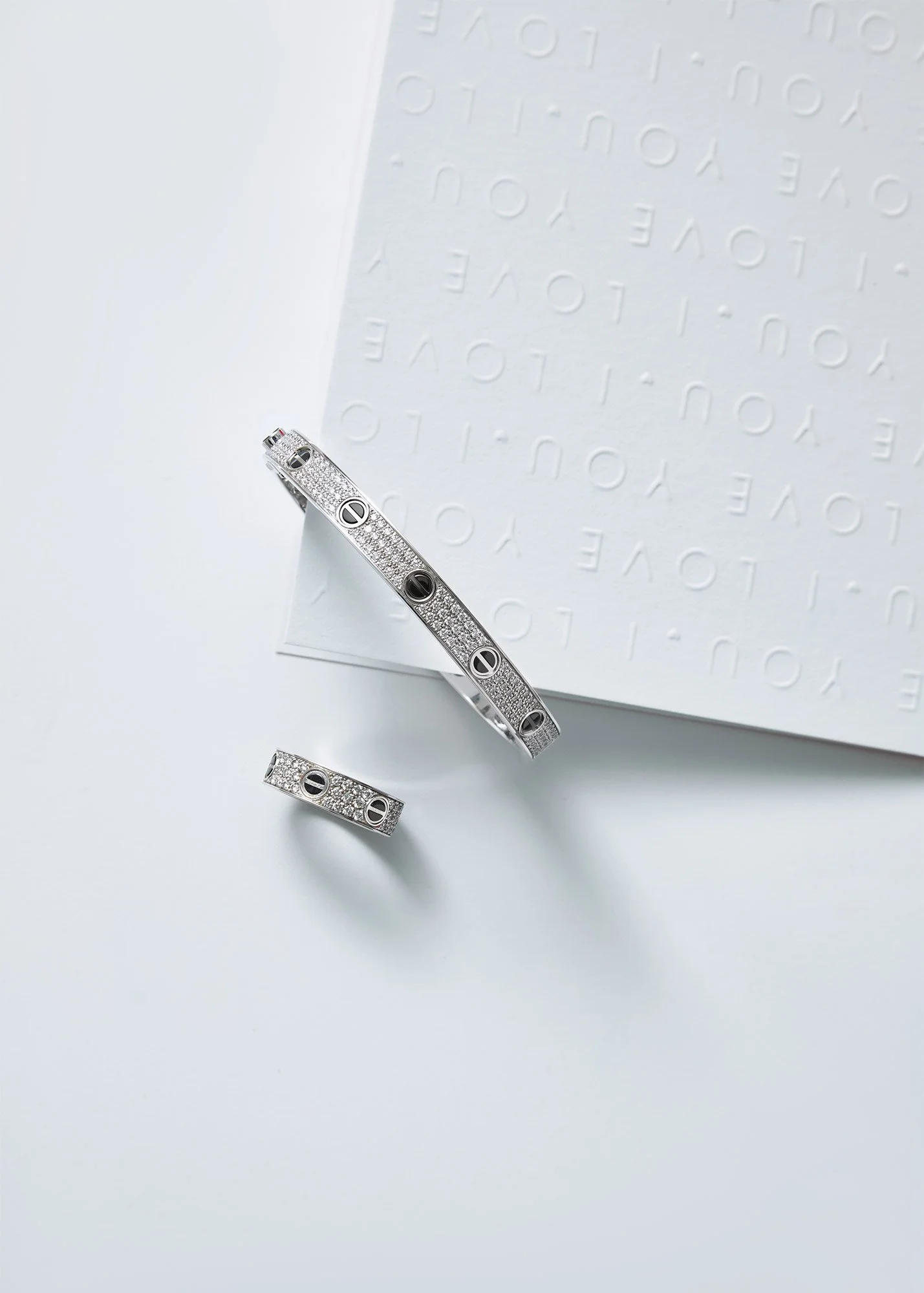 A silver jewelry set consisting of a banglet and a ring, both encrusted with small diamonds and featuring black circular accents, placed on a white surface with a textured paper in the background.