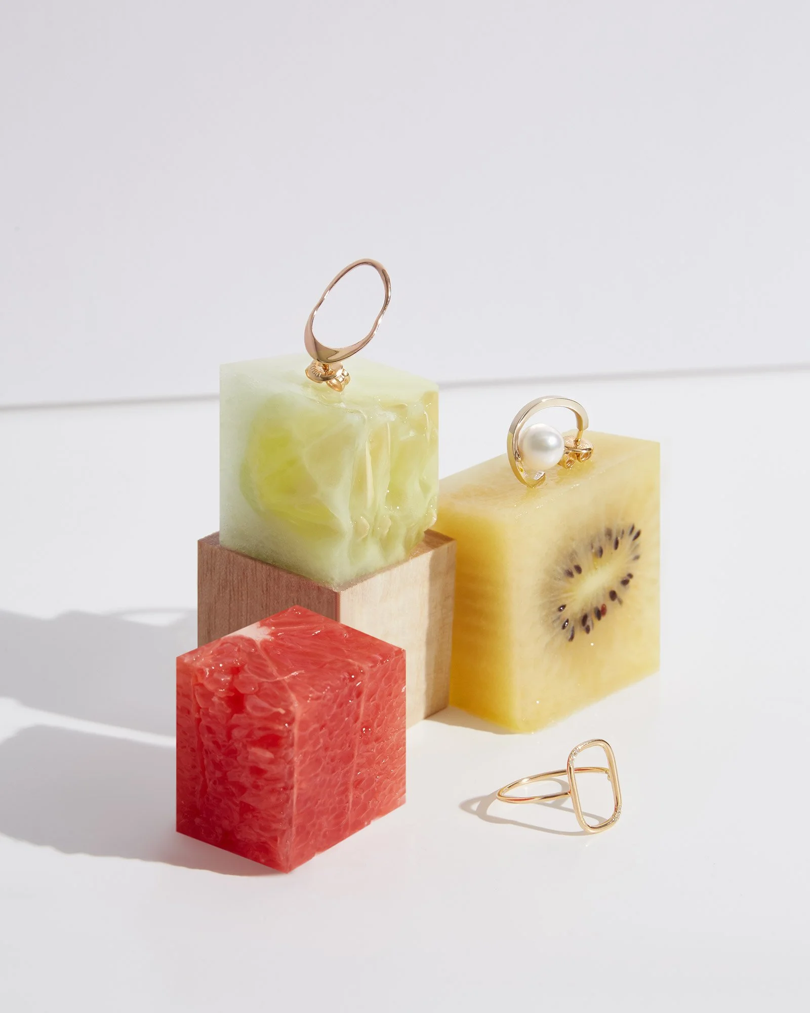 Jewelry rings displayed on colorful fruit-shaped soap blocks arranged on a white surface.