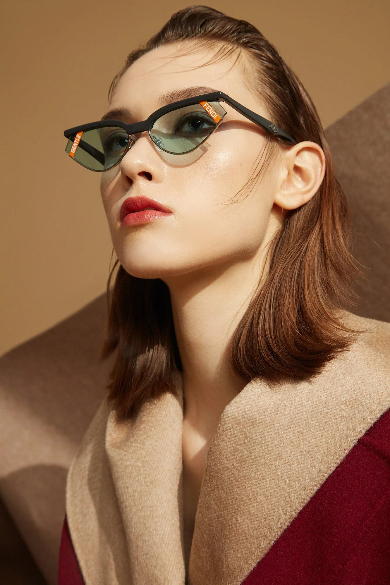 A woman with short brown hair wearing stylish eye glasses with green tinted lenses and the labels 'FENDI' and 'CELINE' on the frames, against a neutral background.