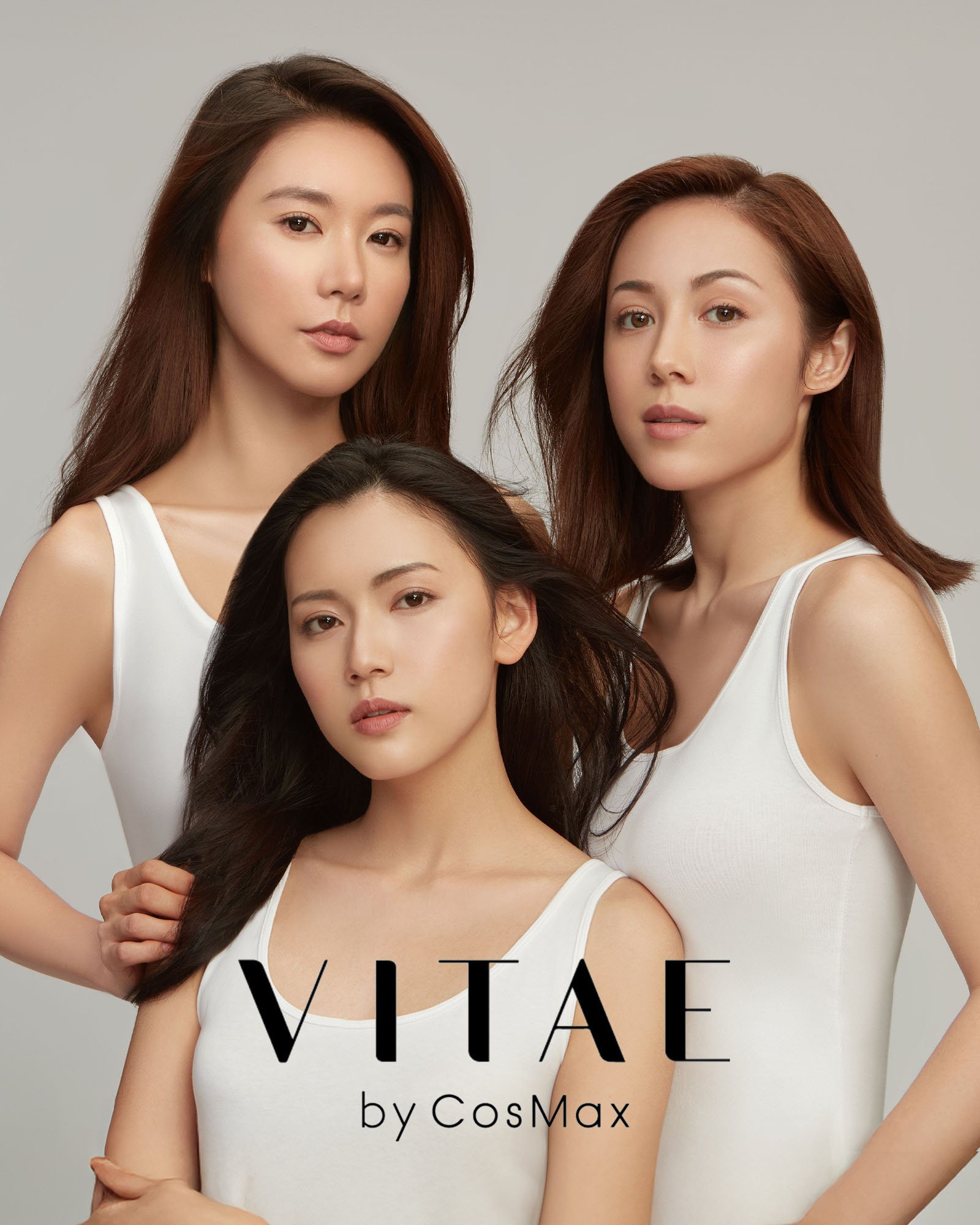 Three women with long hair wearing white tops posing against a gray background.