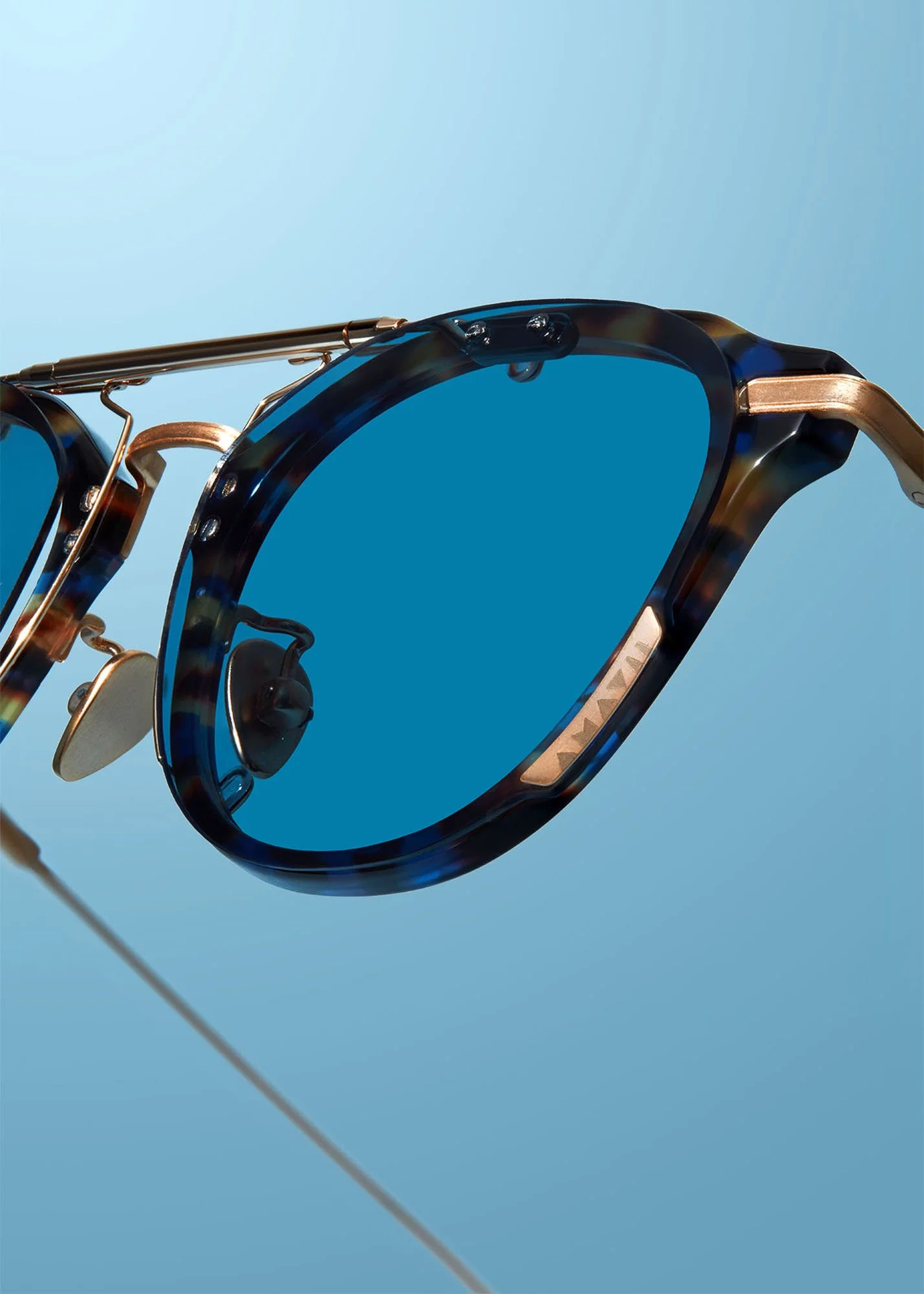 Close-up of designer sunglasses with tortoiseshell frame and dark lenses, reflecting sunlight against a clear blue sky.