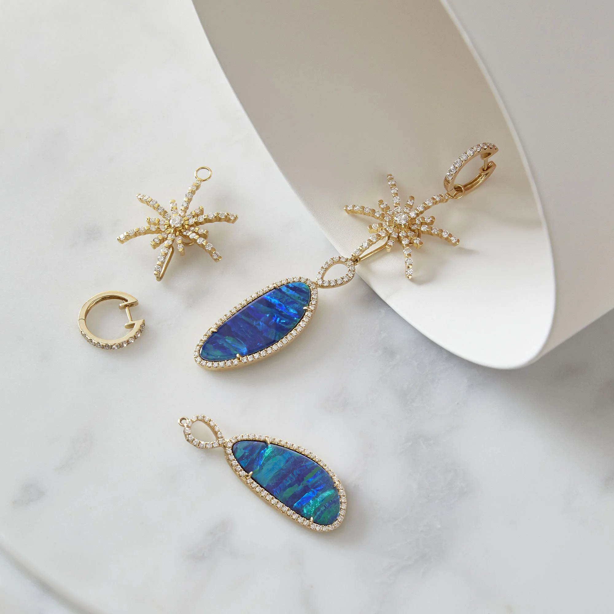 Gold jewelry set including a pair of starfish earrings, a ring, and two matching pendants with blue opal stones and diamond accents, displayed on a white surface with a mirror.