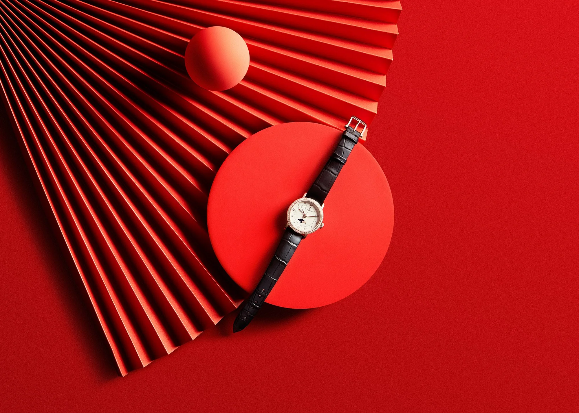 A round white watch with a black leather strap placed on a red circular display, with a red background and geometric red elements surrounding it.