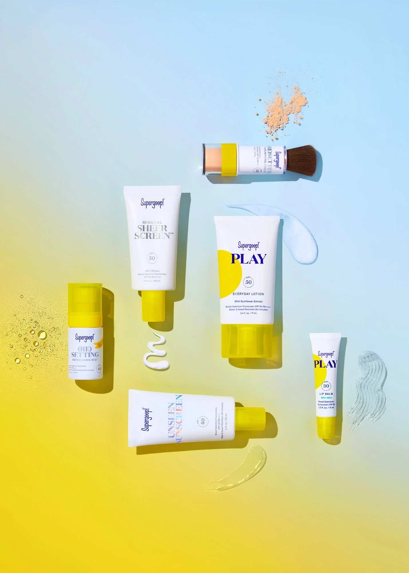 Collection of Supergoop! skincare products on yellow and blue background, including sunscreen lotions, setting spray, lip balm, face sunscreen, brush, and swatch of product.