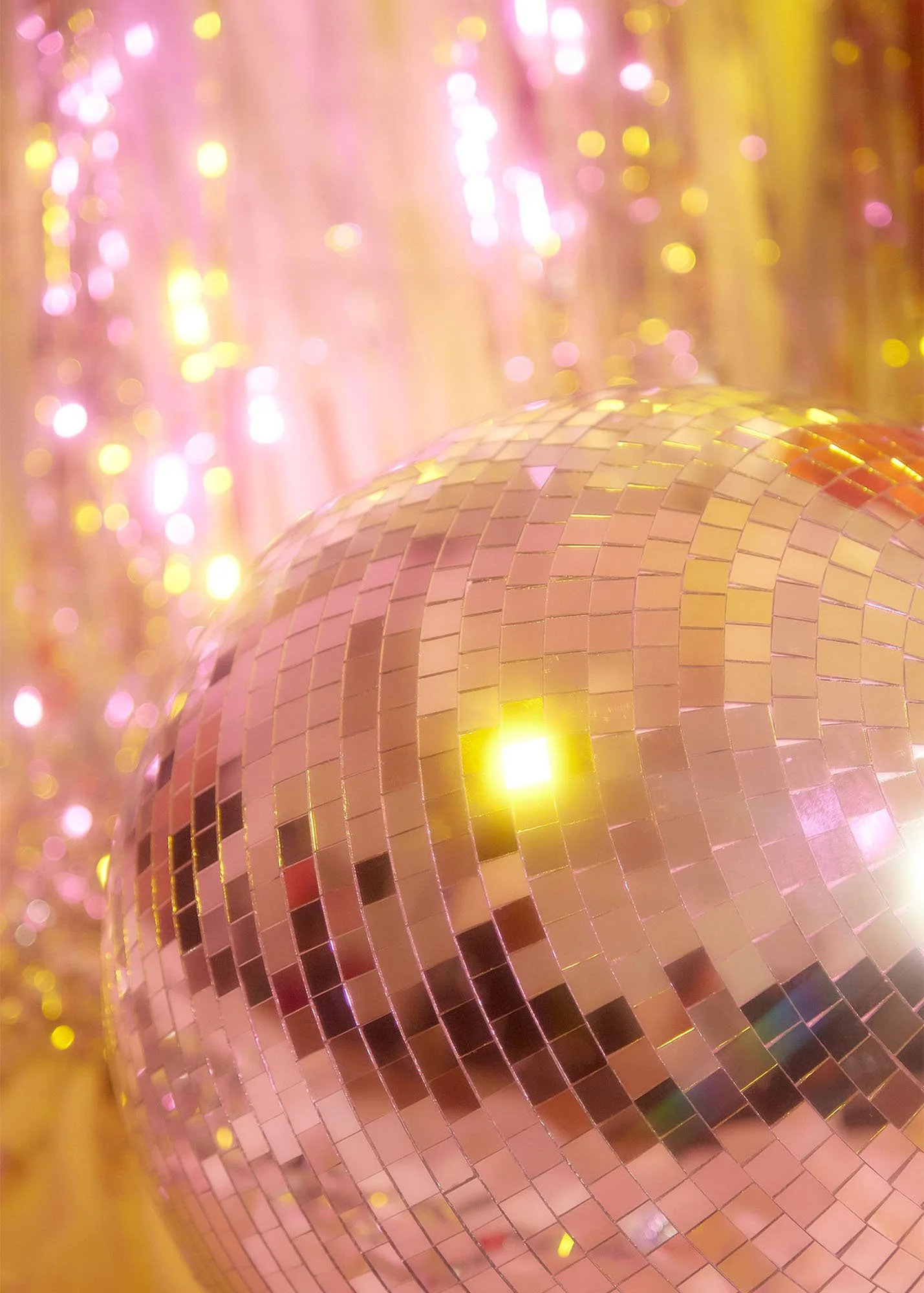 Close-up of a large disco ball reflecting yellow and pink lights, with a shimmering golden curtain in the background.
