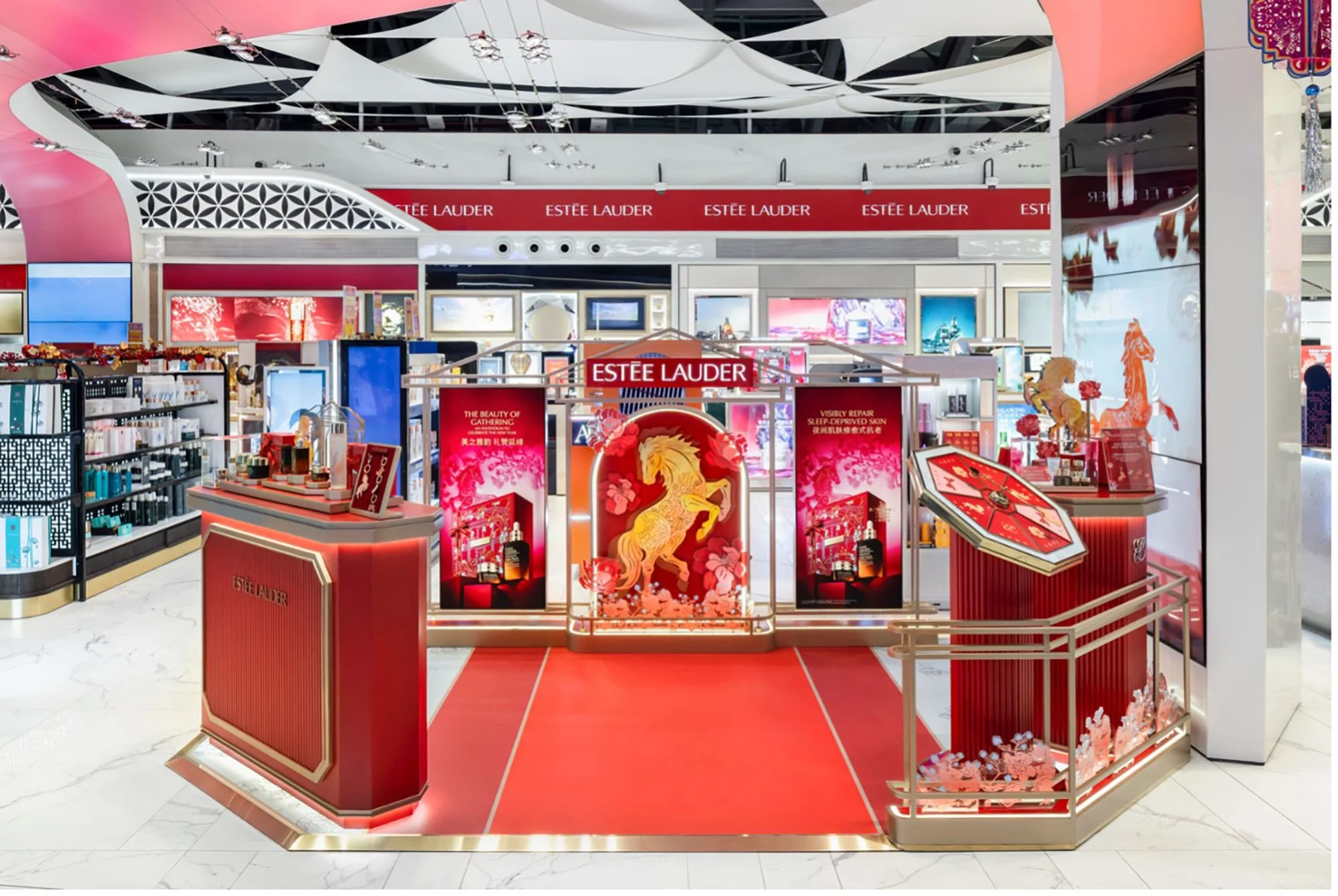 A retail display for Estée Lauder cosmetics with red and gold accents, featuring an artistic depiction of a lion and floral patterns, set within a mall.