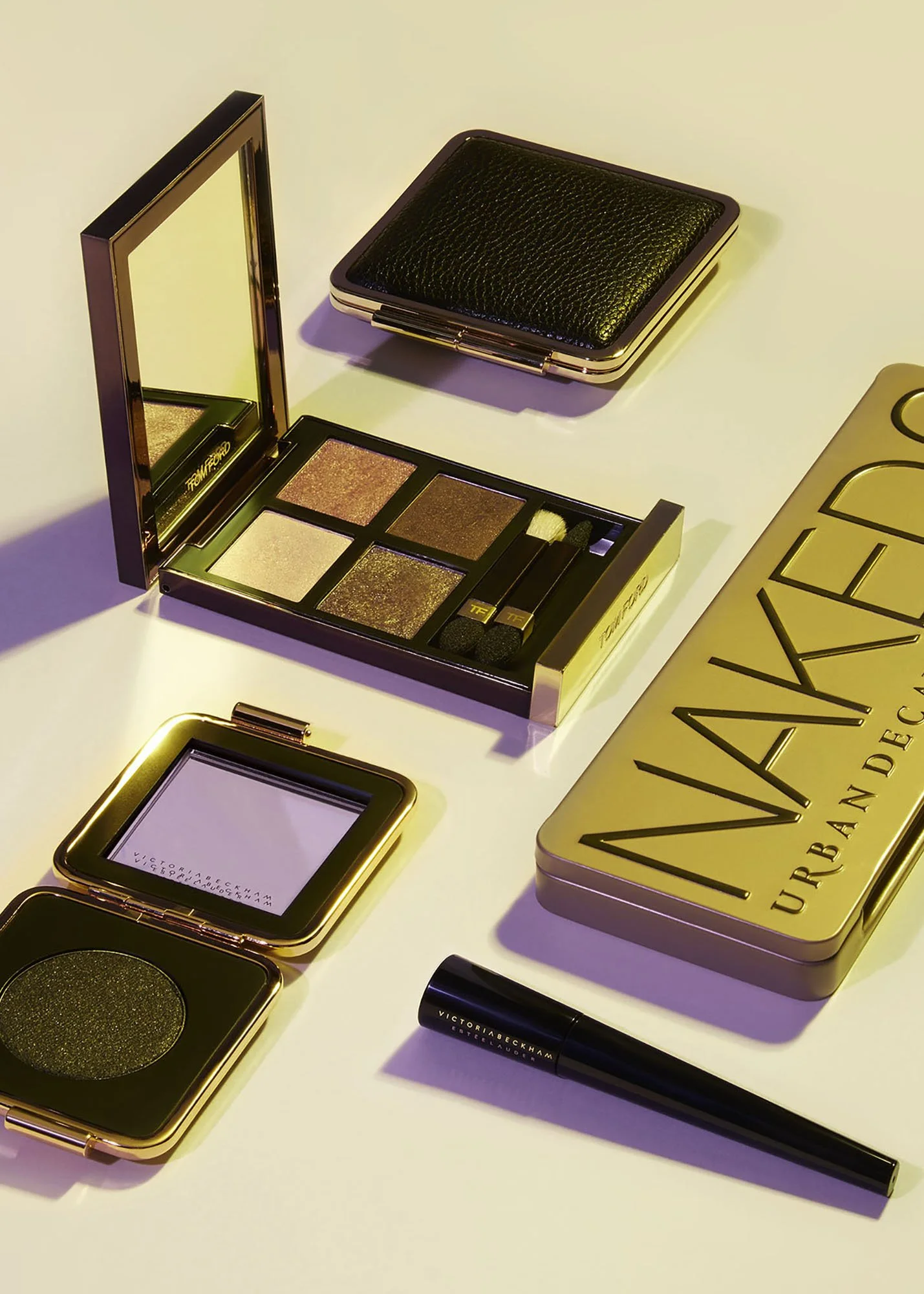 Collection of Victoria Beckham makeup products, including an eyeshadow palette, compact mirror, lip gloss, and a small black case on a white surface.