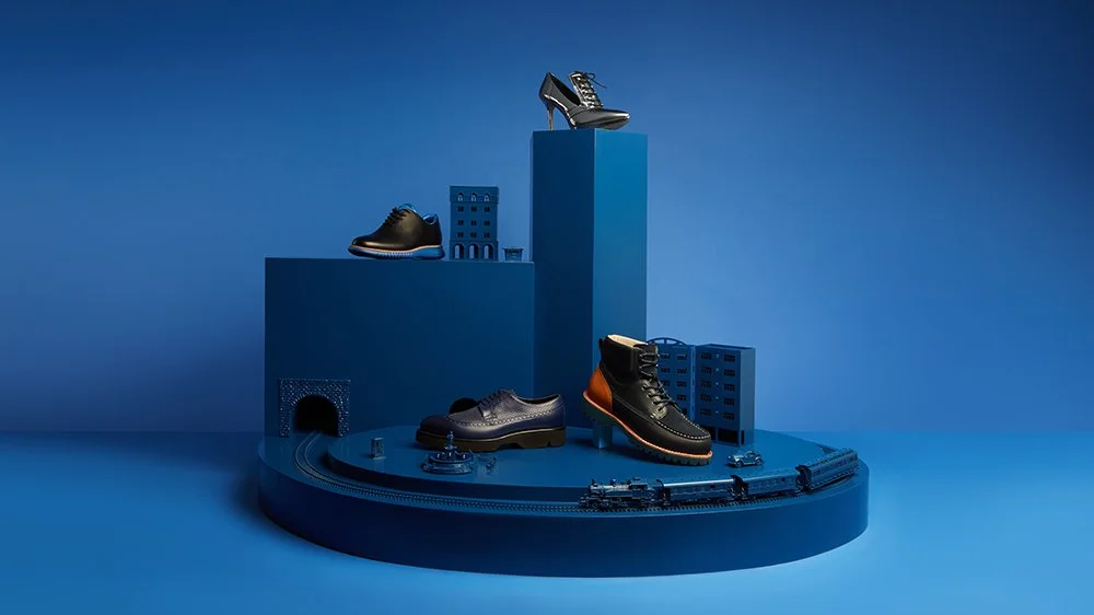 Display of shoes on blue platforms with model train and cityscape details on a blue background.