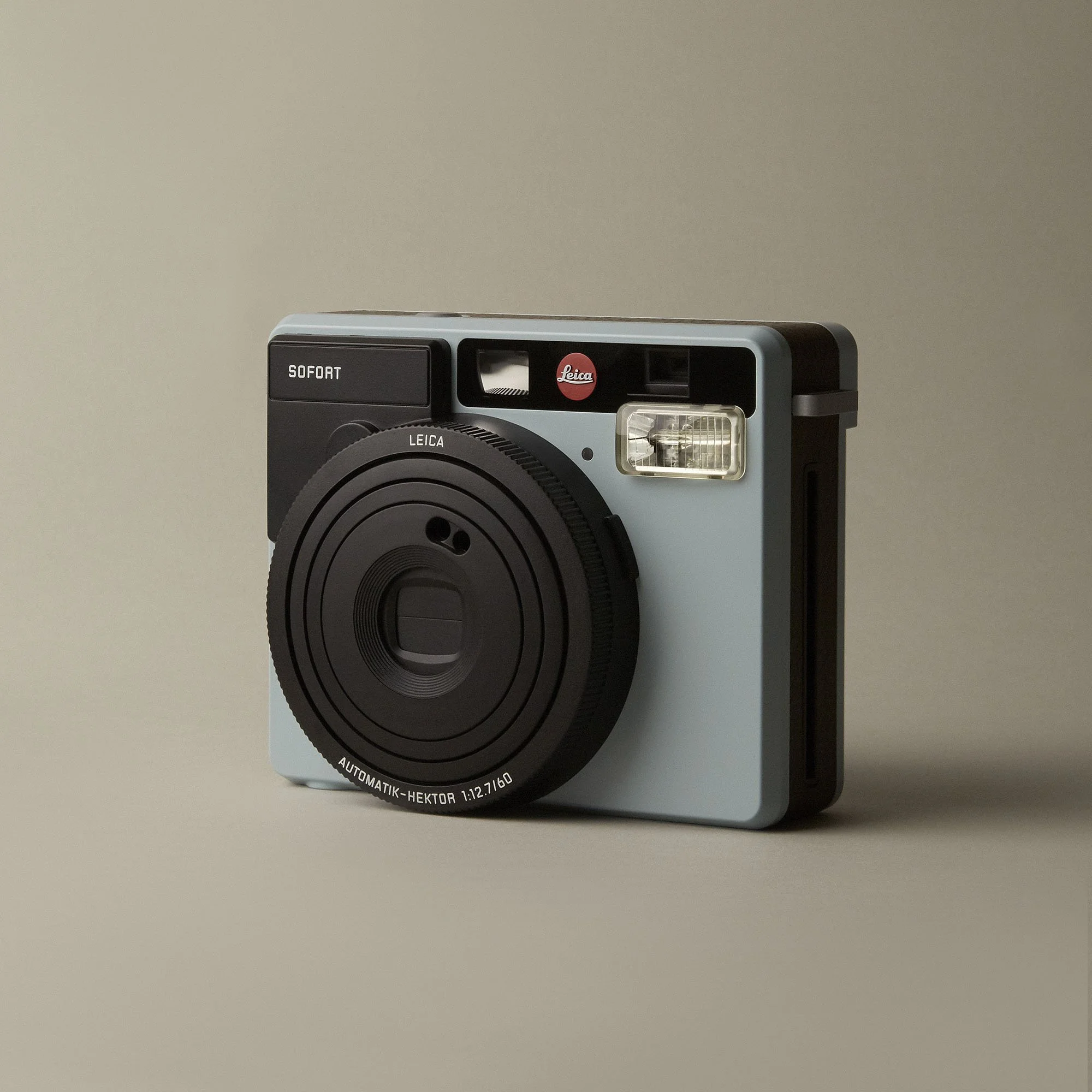A vintage instant camera with a light blue body and black accents, featuring a prominent lens and a viewfinder, with the Leica logo visible on the top right.
